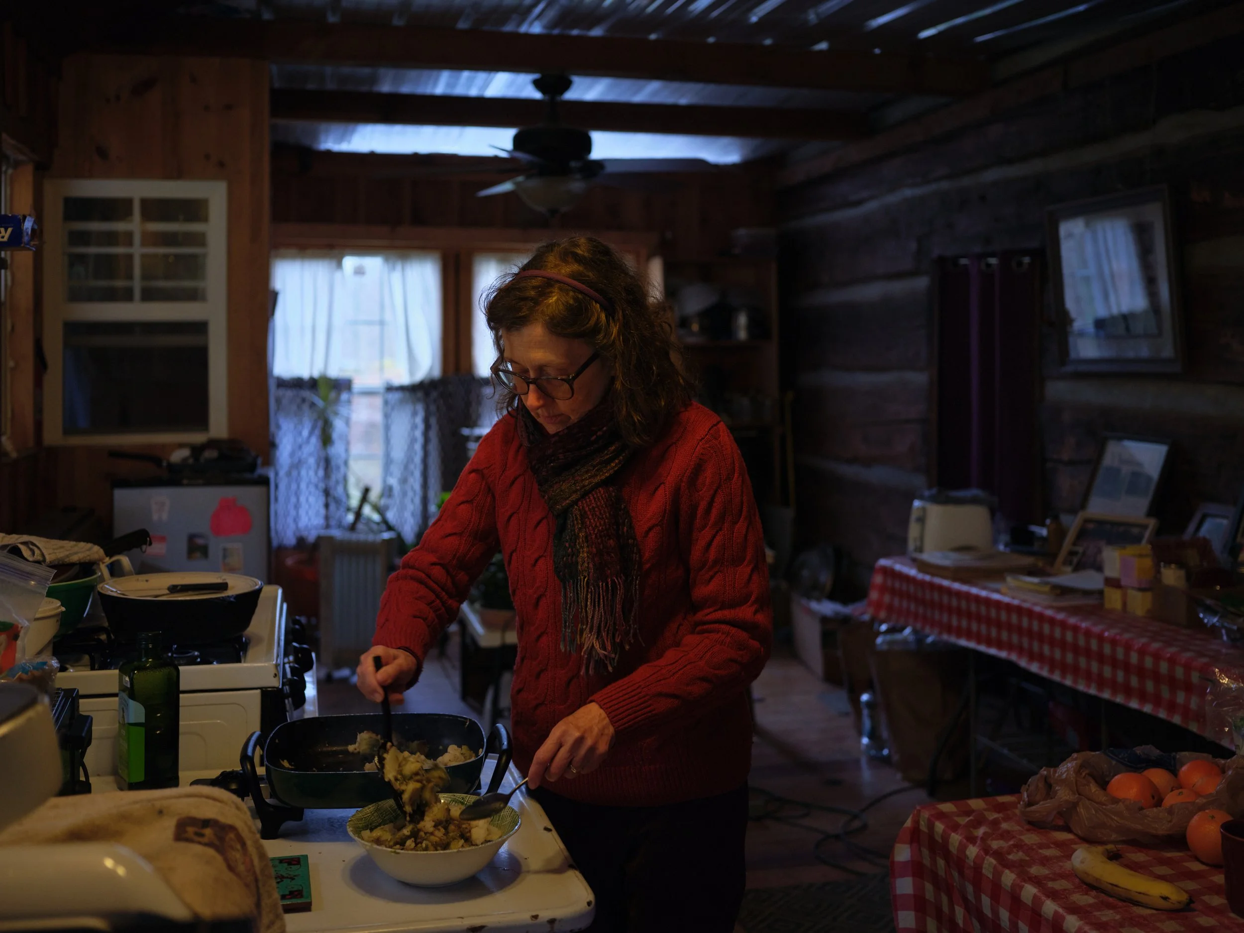 A woman wearing glasses, a red sweater, and a colorful scarf prepares food.