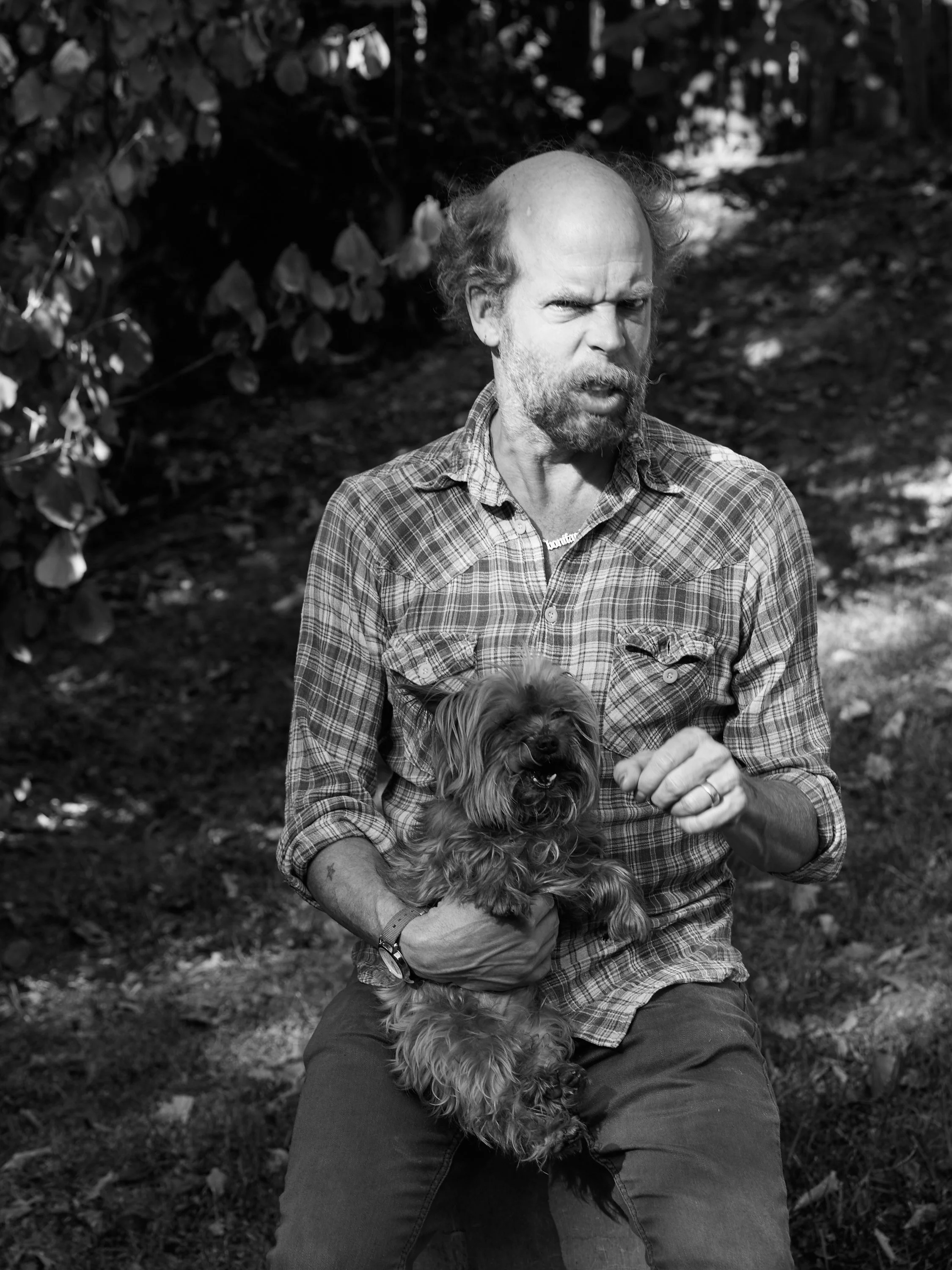 A black-and-white photo of a person holding a small dog in their lap outdoors.