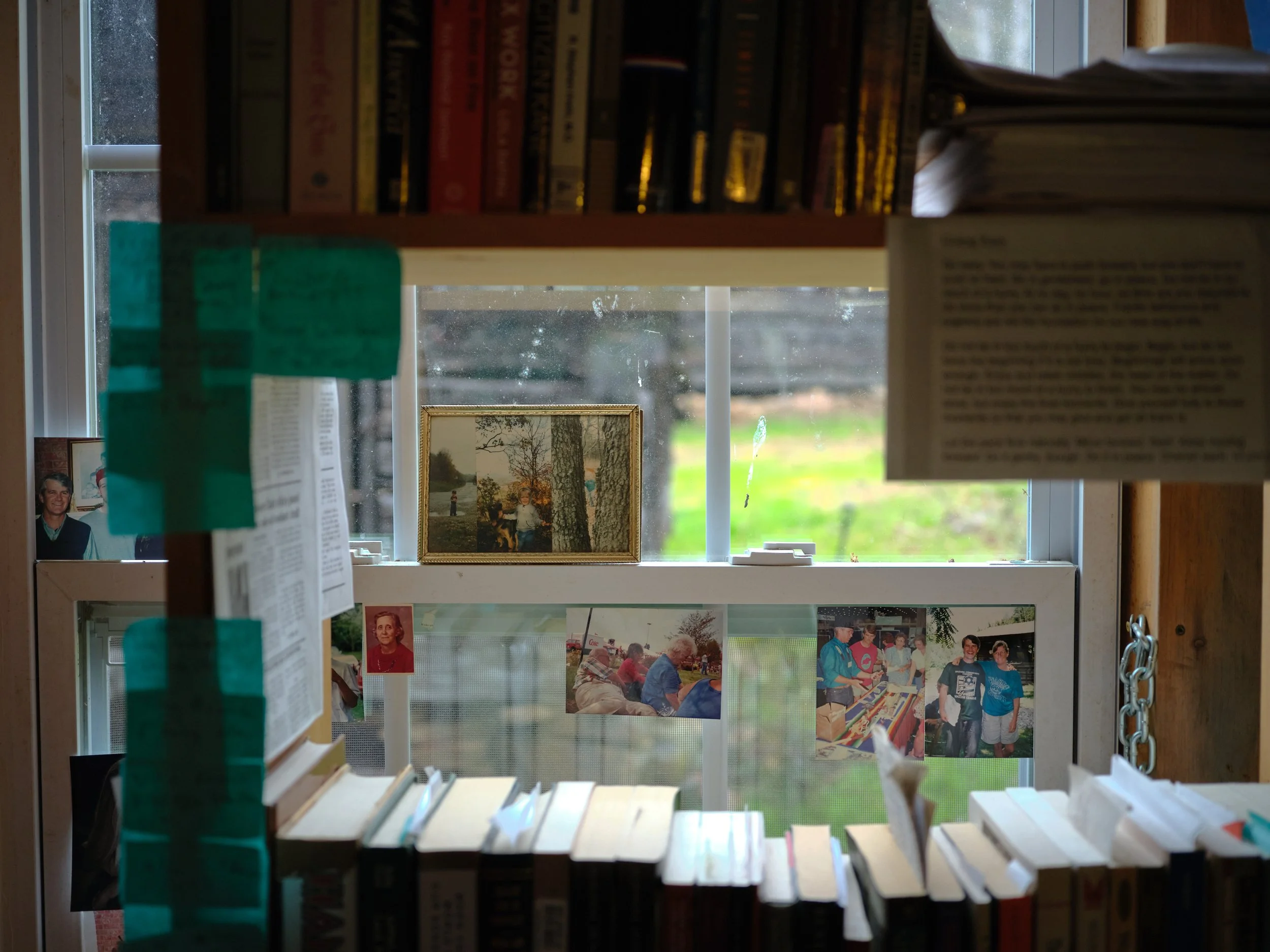 A window with books and photographs on the windowsill and bookshelf.
