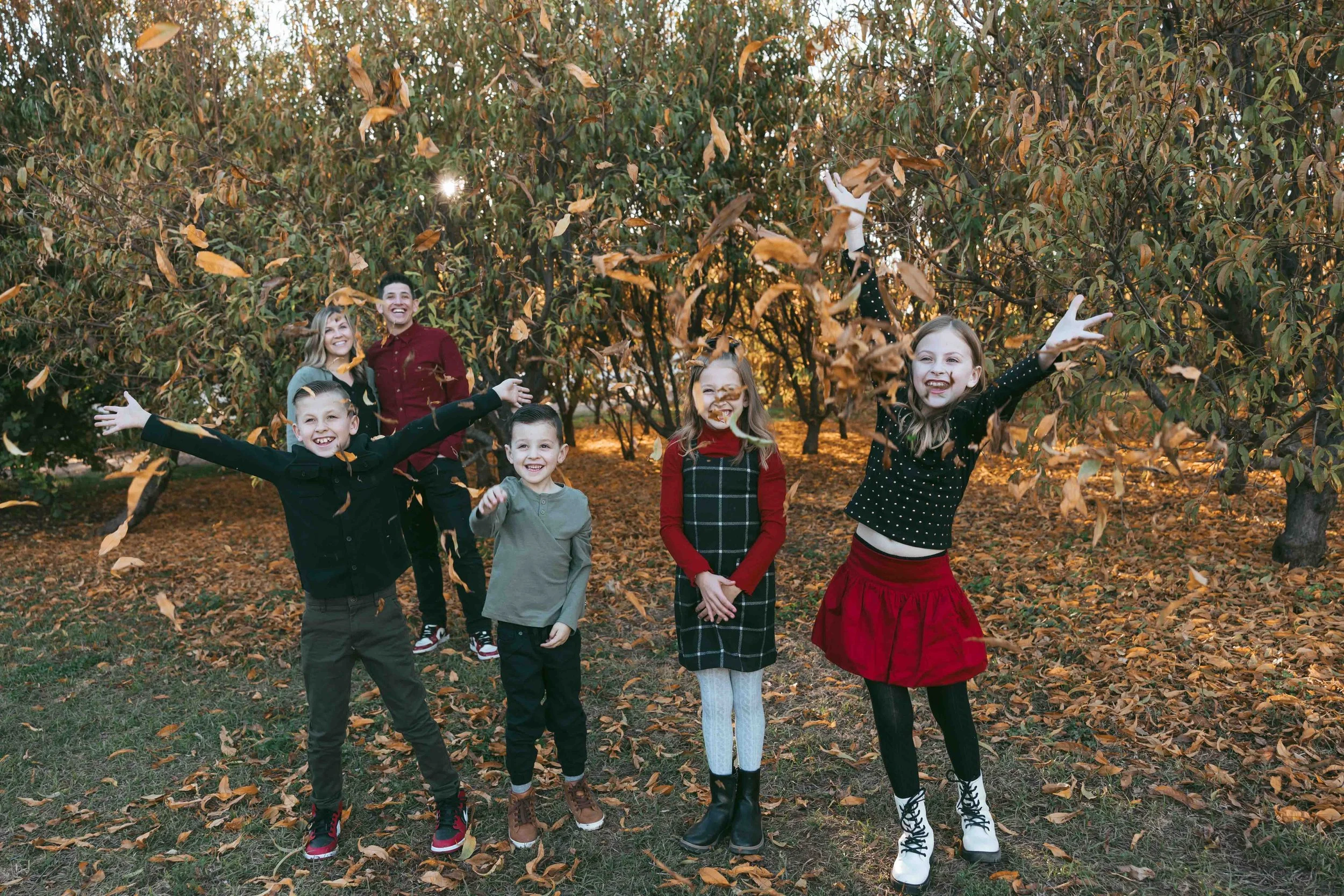 Four siblings playing in fall leaves at Agritopia Orchard Gilbert