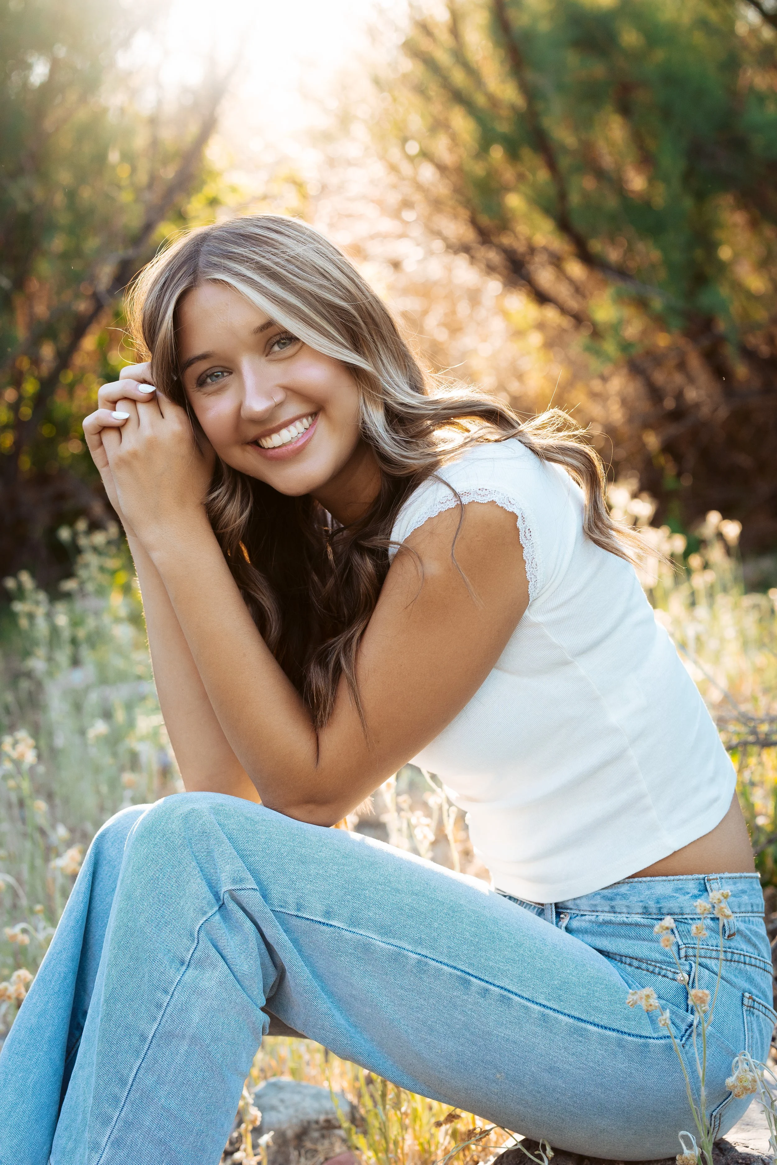 Blonde young lady smiling in the wild flowers with the sun behind her