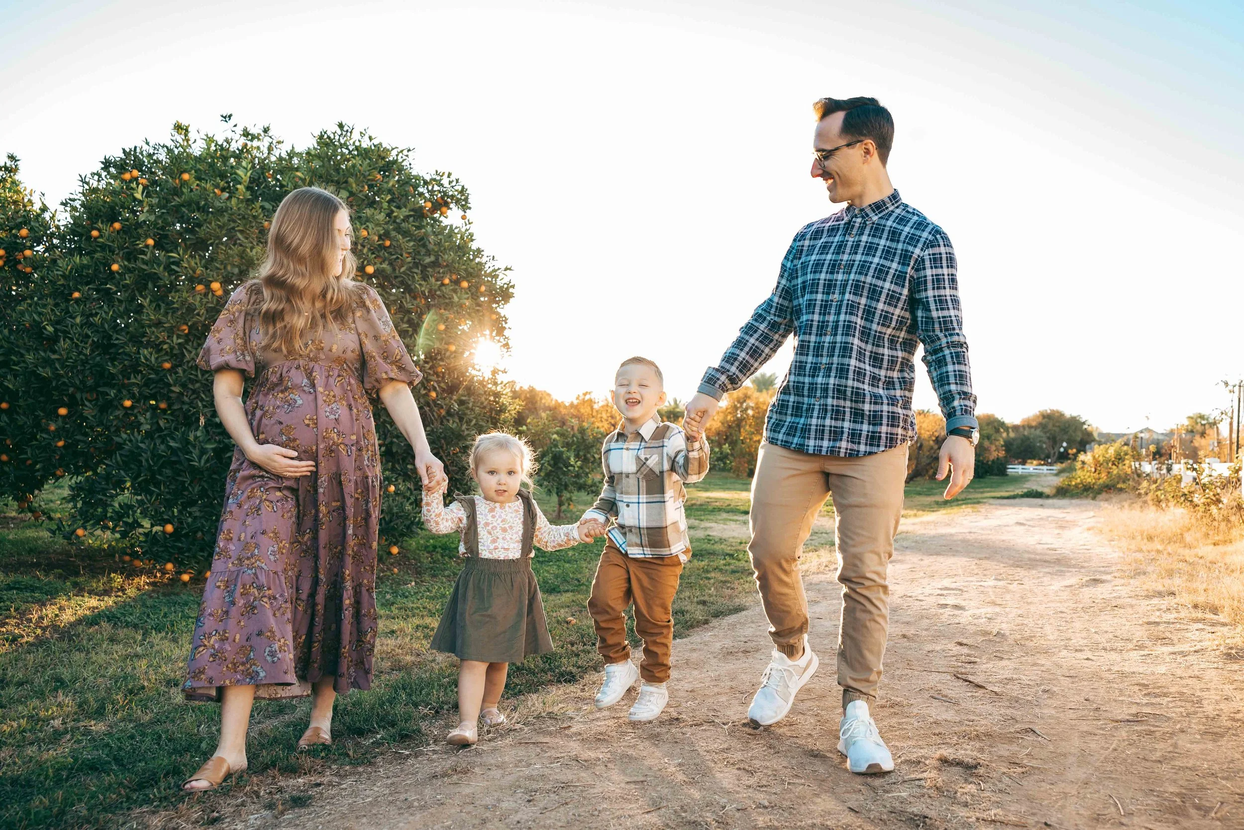 Gilbert family photographer capturing parents and toddlers walking together at Agritopia Orchard during sunset
