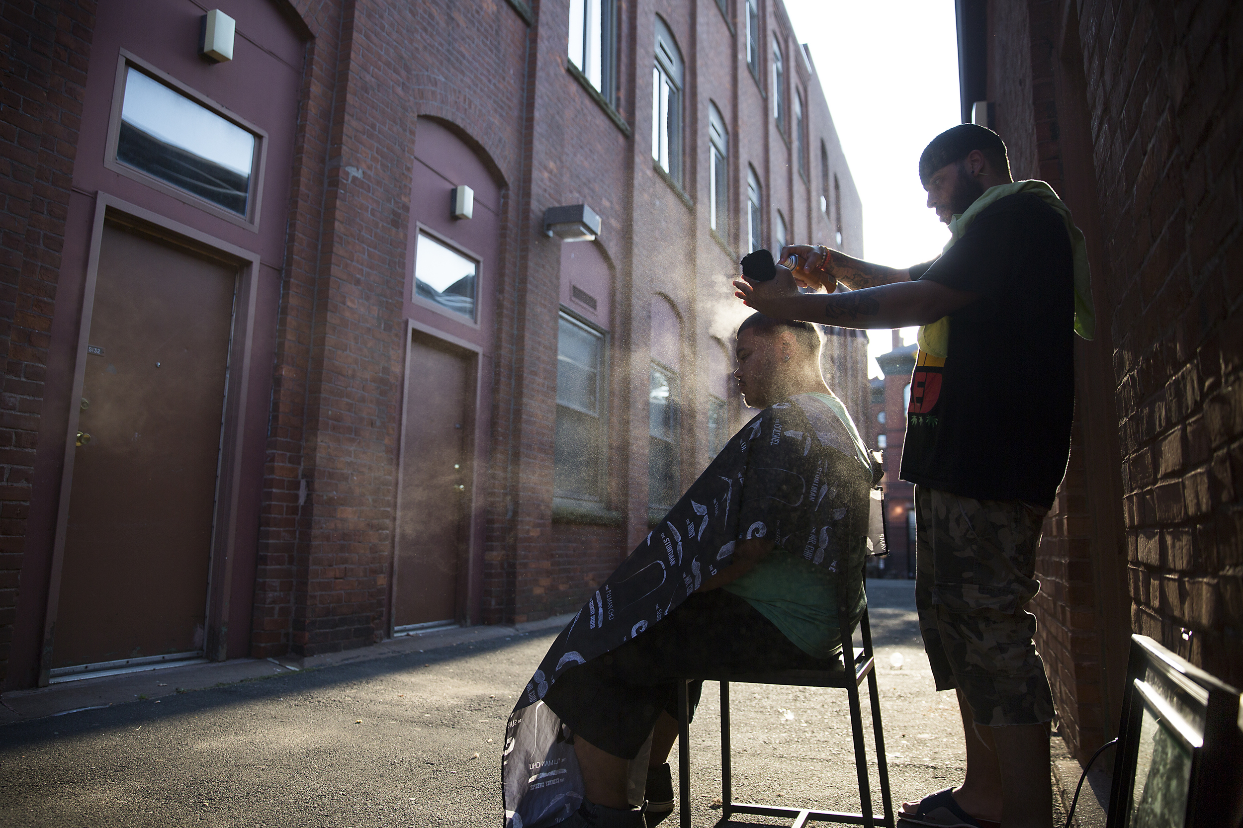 Lee Medina cuts Carlos Morales' hair in the alley in front of his Billings Forge apartment in Hartford, Connecticut. "This is the best place to get a hair cut," said Morales, who met Medina through his own father who also gets his hair cut by him. Medina is a barber and a dancer and has been cutting hair for the community in Billings Forge since he moved into his apartment two years ago. 