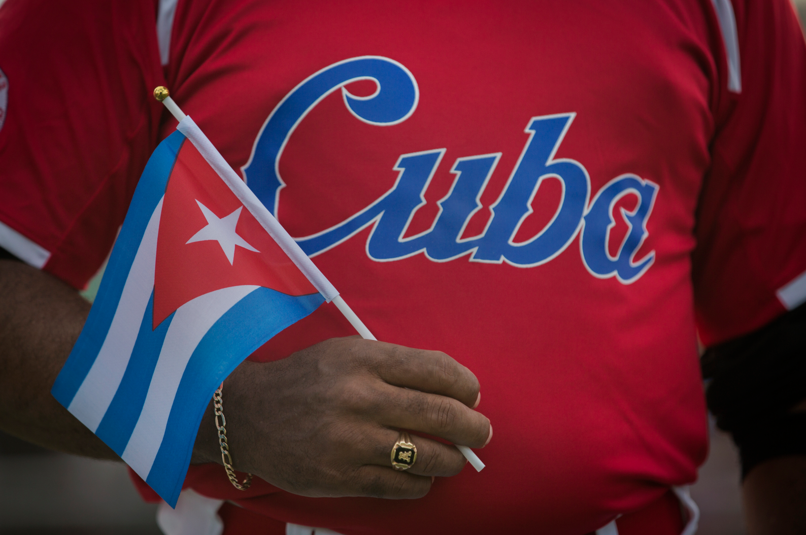 Julio Fernandez, a coach for the Cuba team on the USA-Cuba Goodwill Tour holds a Cuban flag in front of his teams jersey while the Cuban National Anthem plays at the University of Hartford's Fiondella Field. Three months after a group of young baseball players from West Hartford, traveled to Holguin, Cuba, 12 Cuban youngsters came Connecticut to play baseball.