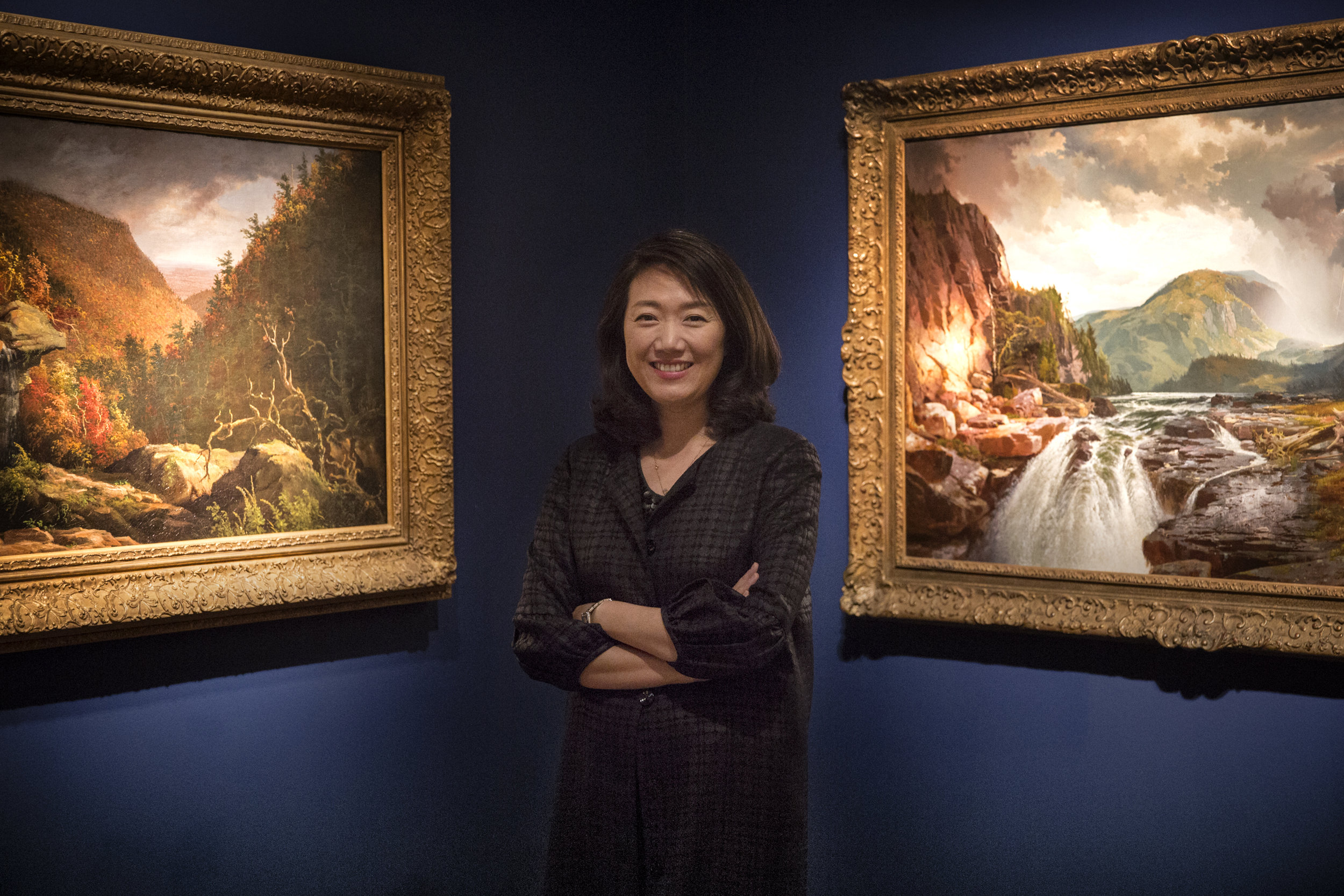 Min Jung Kim, who recently took over as the Director of the New Britain Museum of American Art, stands in the Martin Gallery, next to paintings from the Hudson River School art movement. 