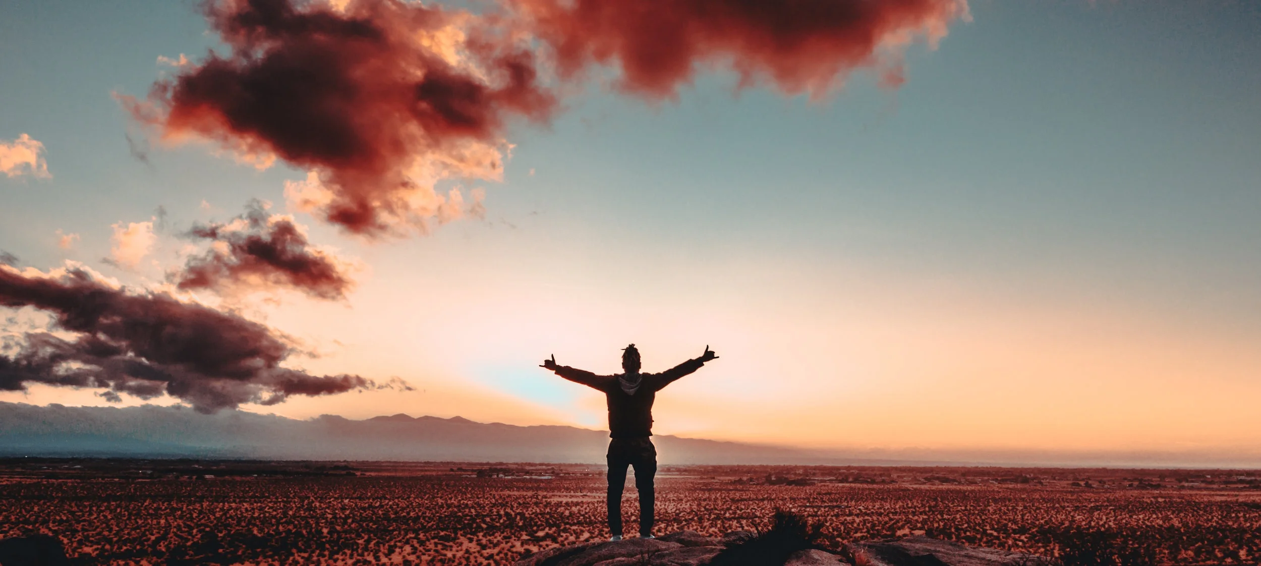 Man stands in a valley, arms spread out in victory