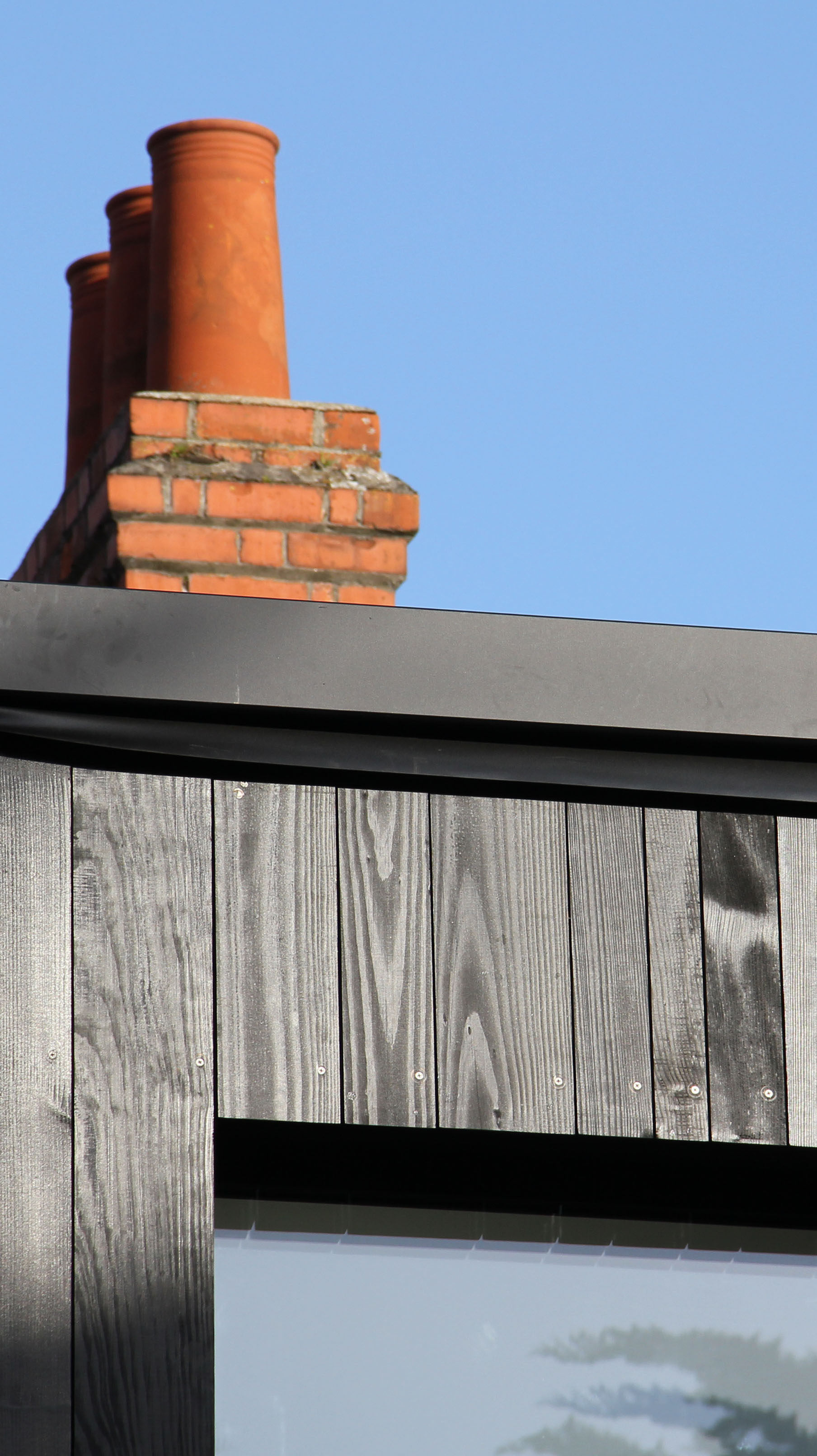 Black stained timber clad extension with old chimney in background