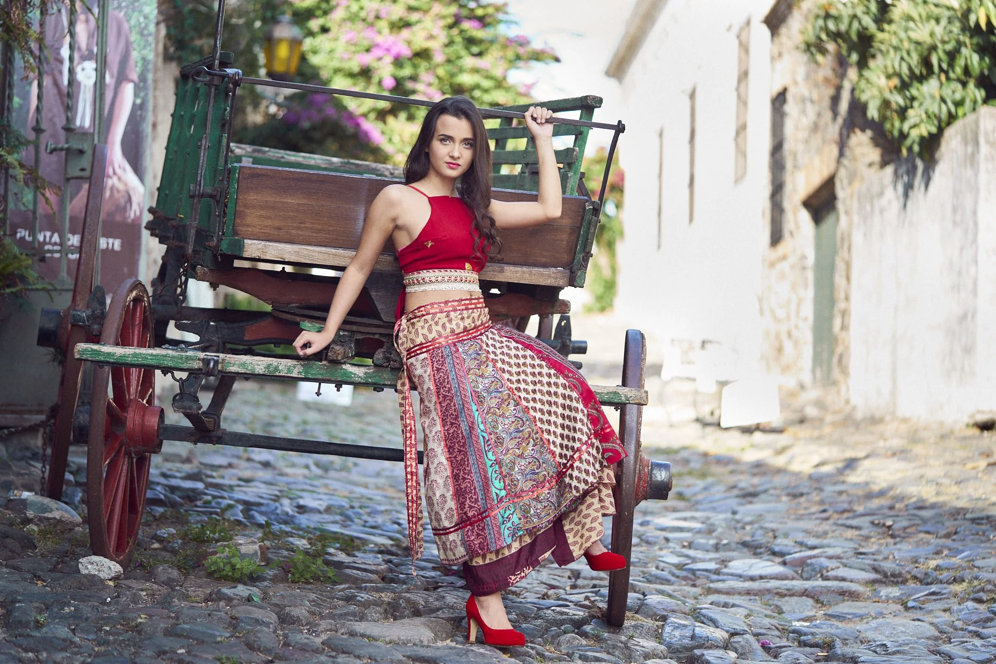Mujer bailando en un callejón cívico de piedra, vestida con ropa tradicional colorida, con un fondo de casas y plantas