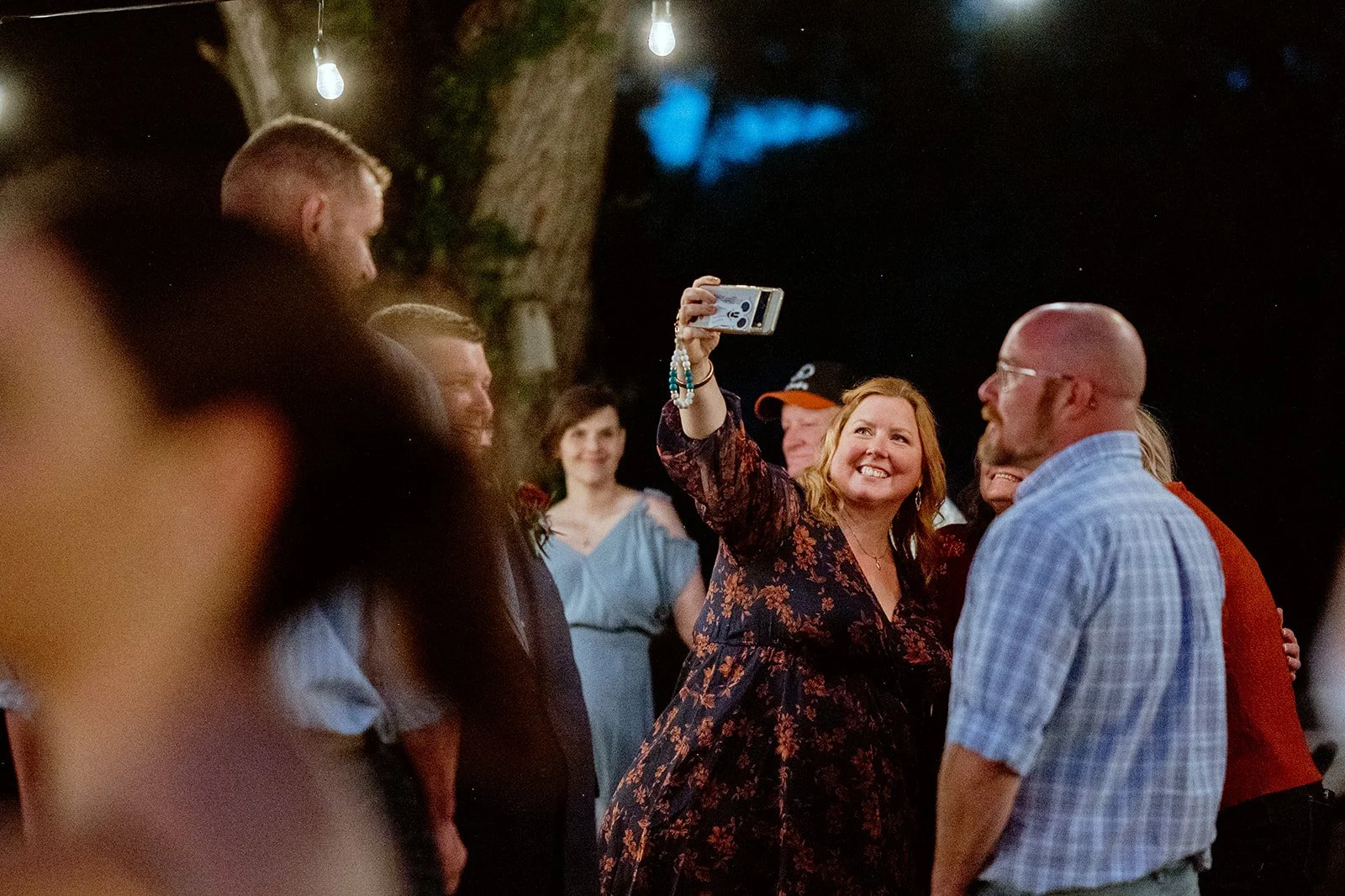 Group of people at a night outdoor gathering, woman taking a selfie.