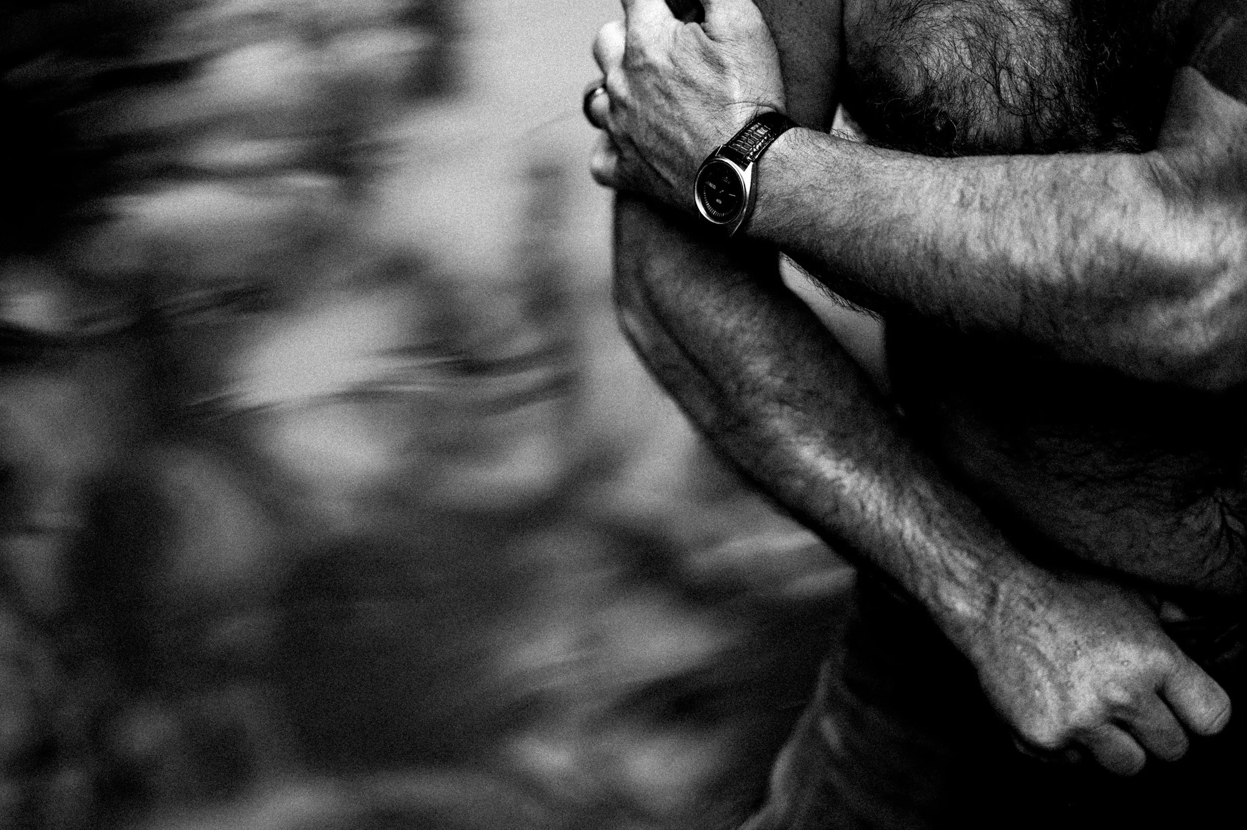 Close-up of a person's arms, one wearing a watch, in a black and white image.