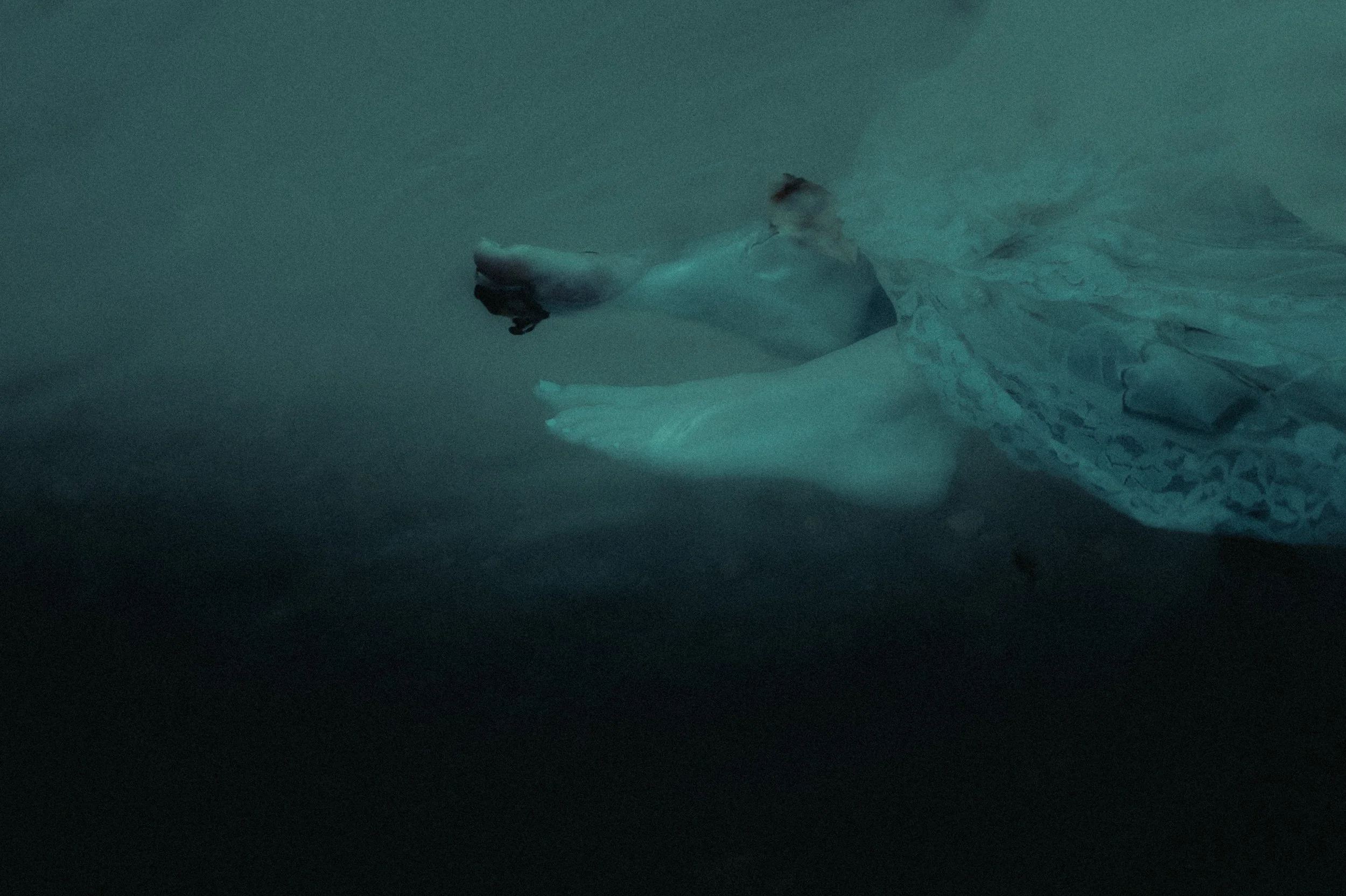 Underwater view of human feet and a lace dress.
