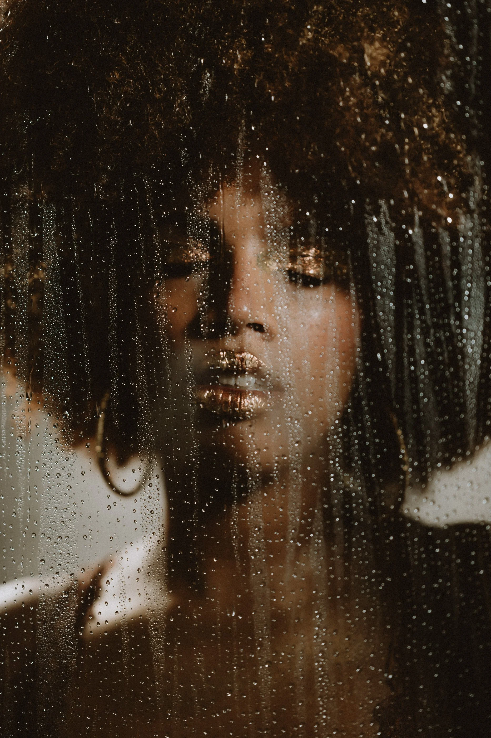Person with curly hair behind wet glass, artistic portrait
