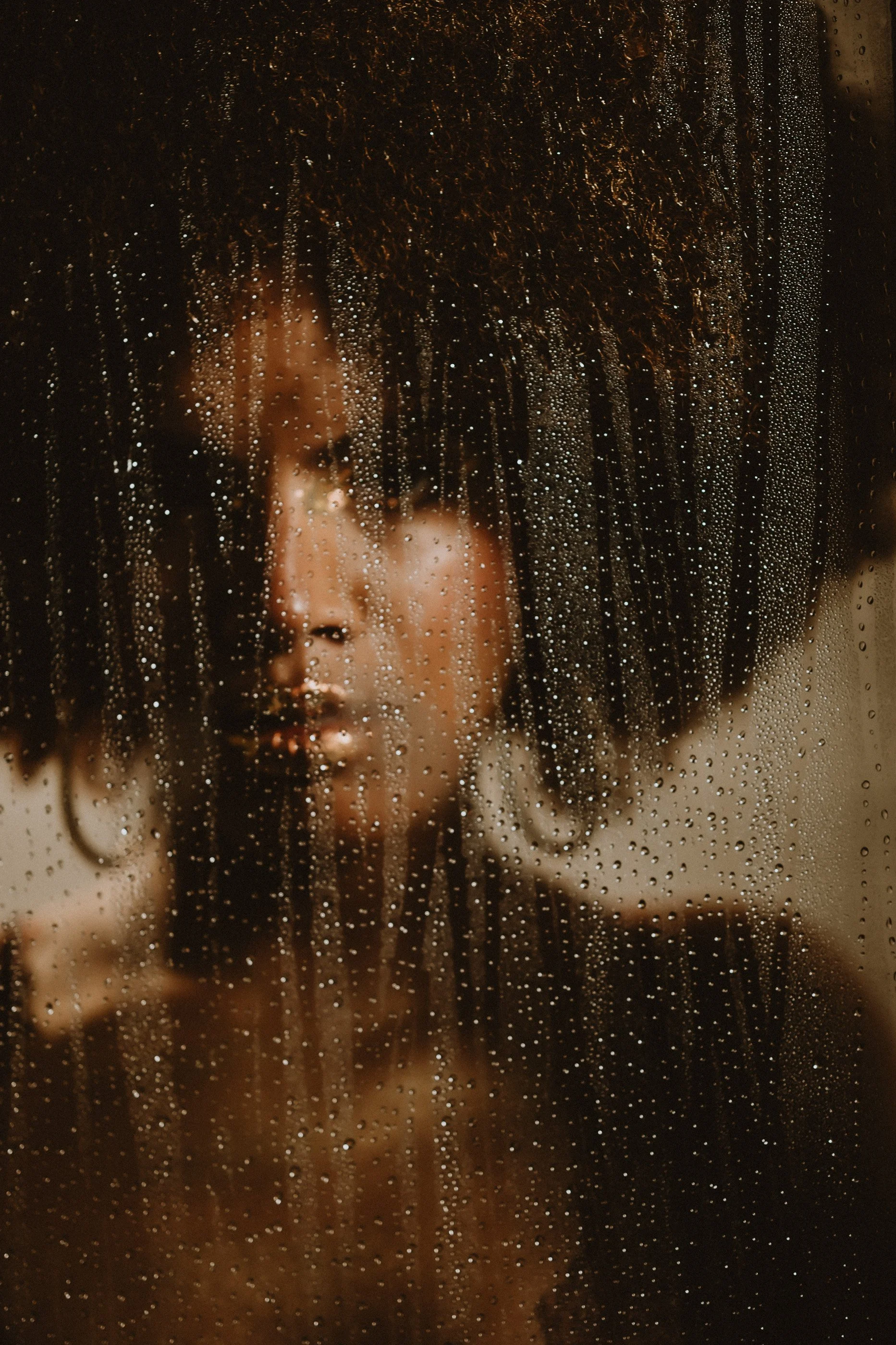 Silhouette of a person behind a wet glass surface, with water droplets.