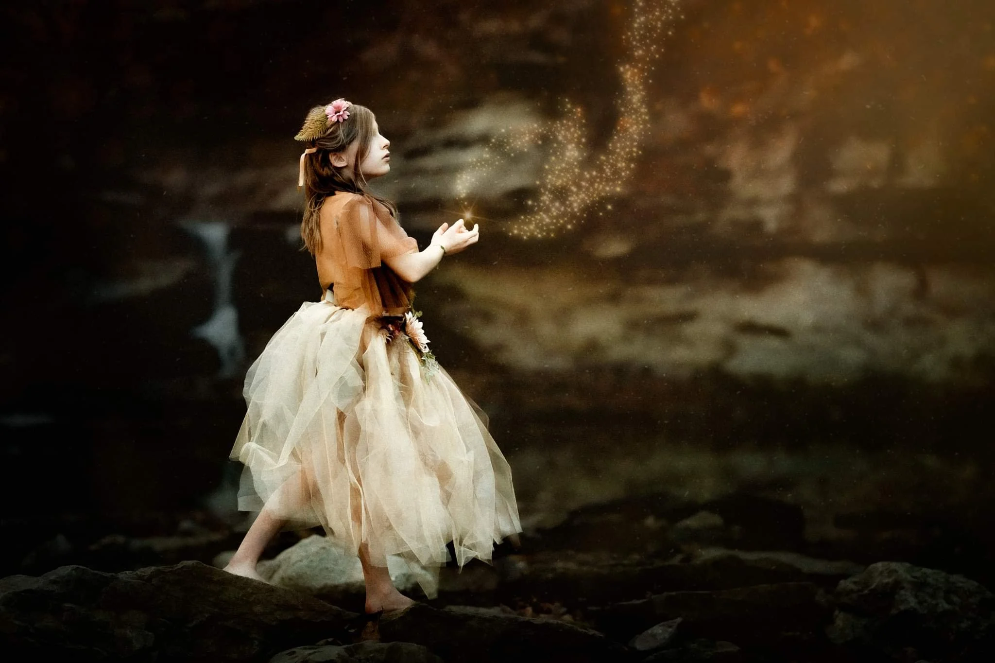 A young girl dressed in a fairy costume stands in a dark woodland environment, reaching out towards a swirl of magical sparkling dust.