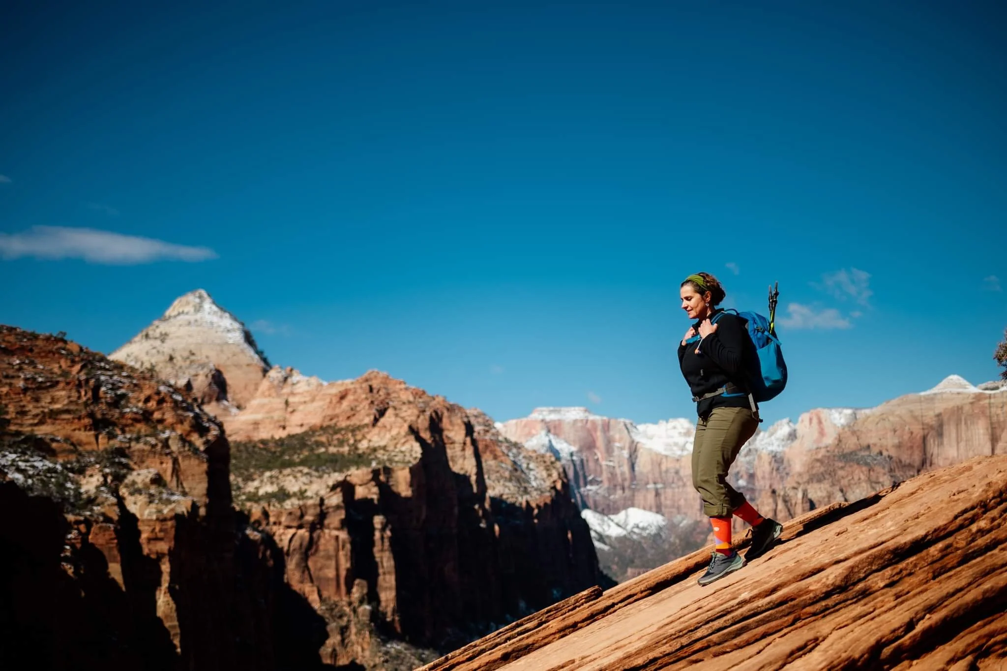 Woman hiking on a rocky slope in a mountainous area with snow-capped peaks and clear blue sky.