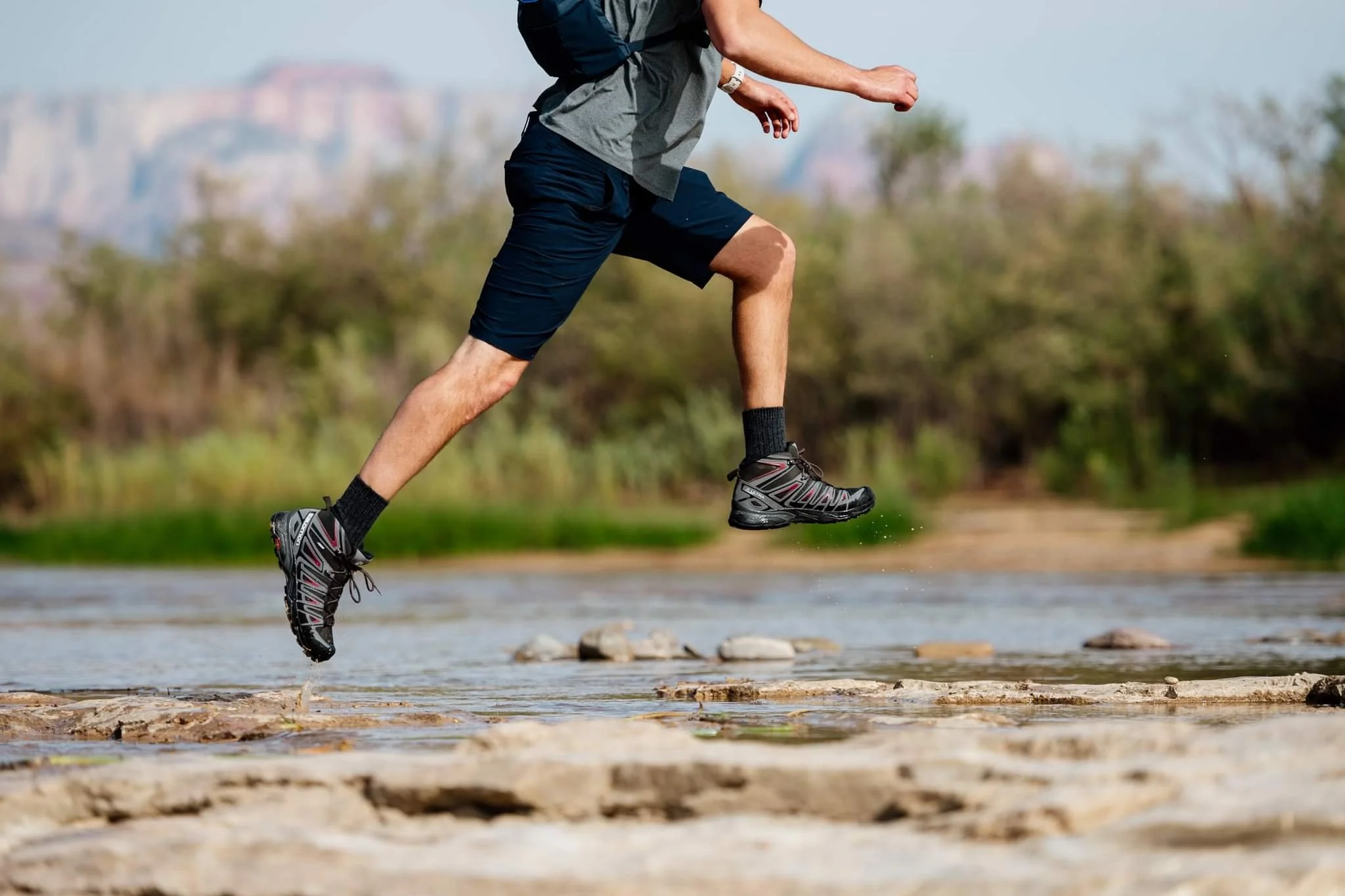 Person wearing hiking shoes jumping over rocks in a river.
