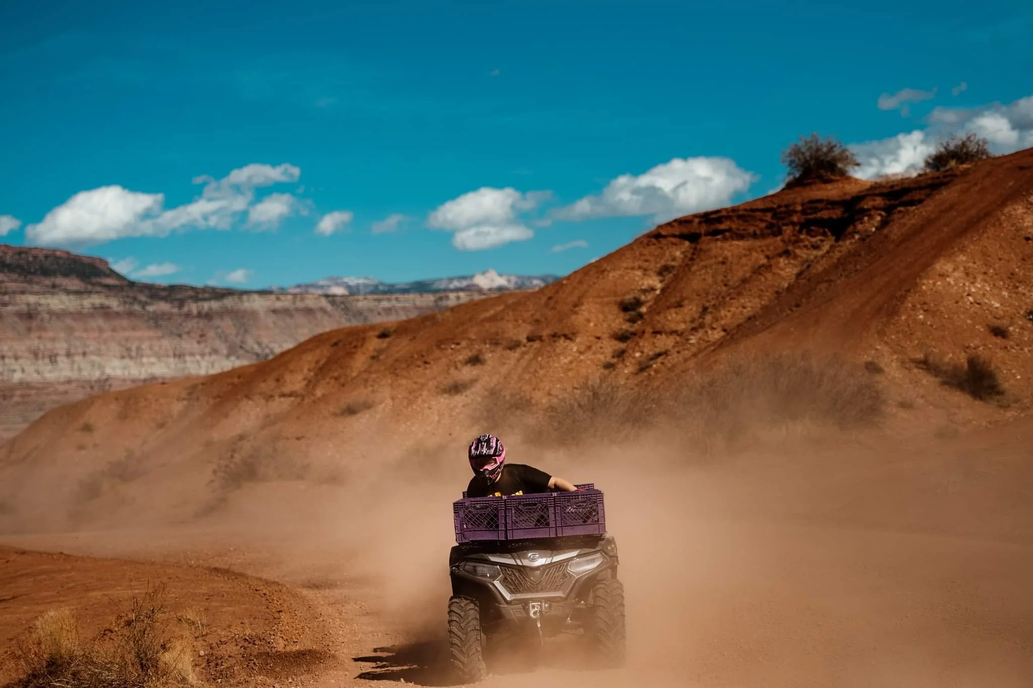 Person riding an ATV on a dusty trail in a desert landscape.