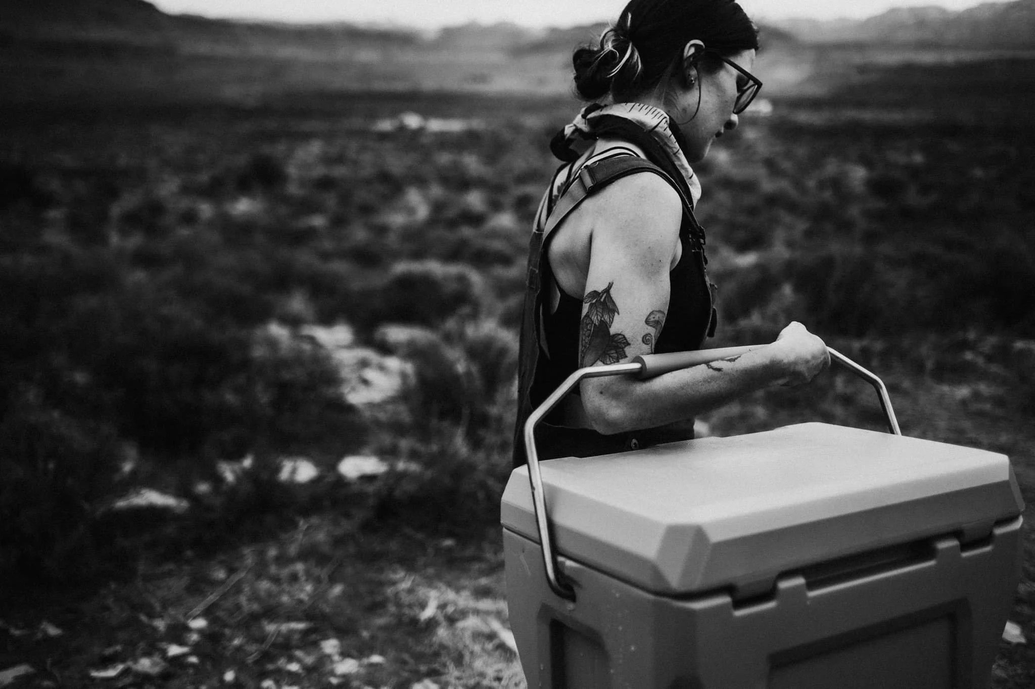 Person carrying a large cooler in a desert landscape, black and white photo