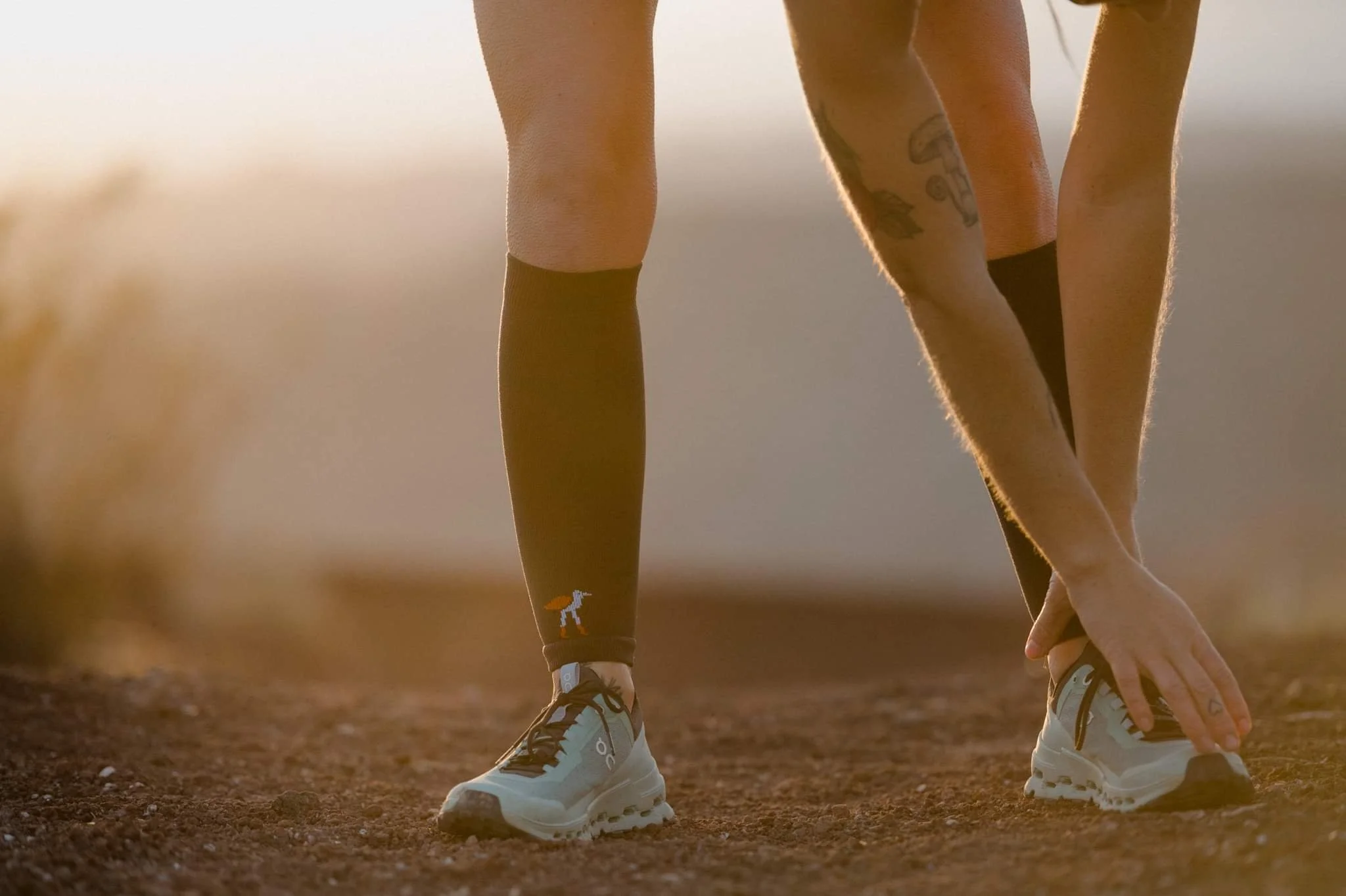 Person wearing black socks and tan running shoes bending over outdoors