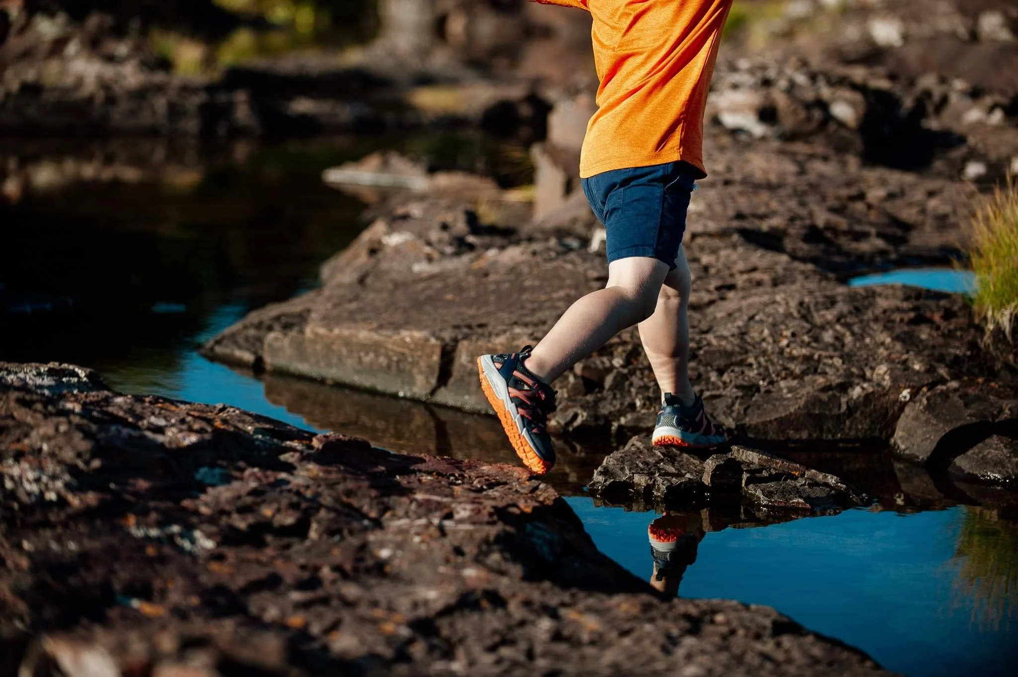 Person wearing an orange shirt and black shorts stepping on rocks near water