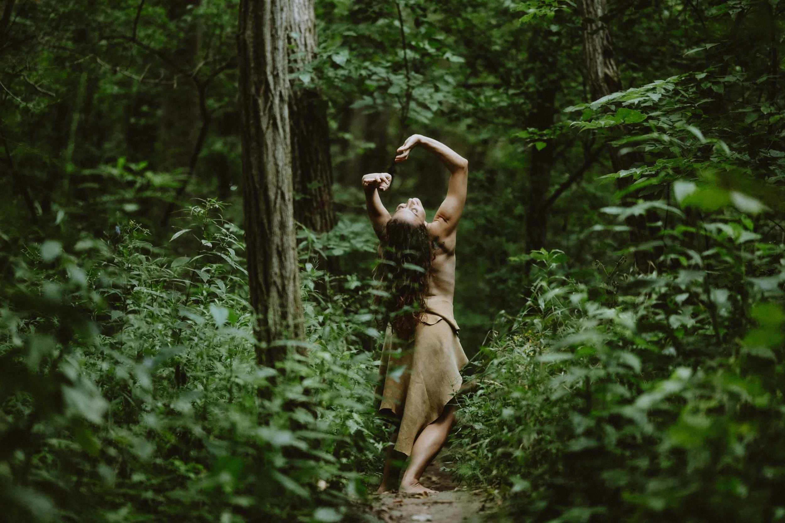 Person dancing in a dense forest, surrounded by lush green foliage and trees.