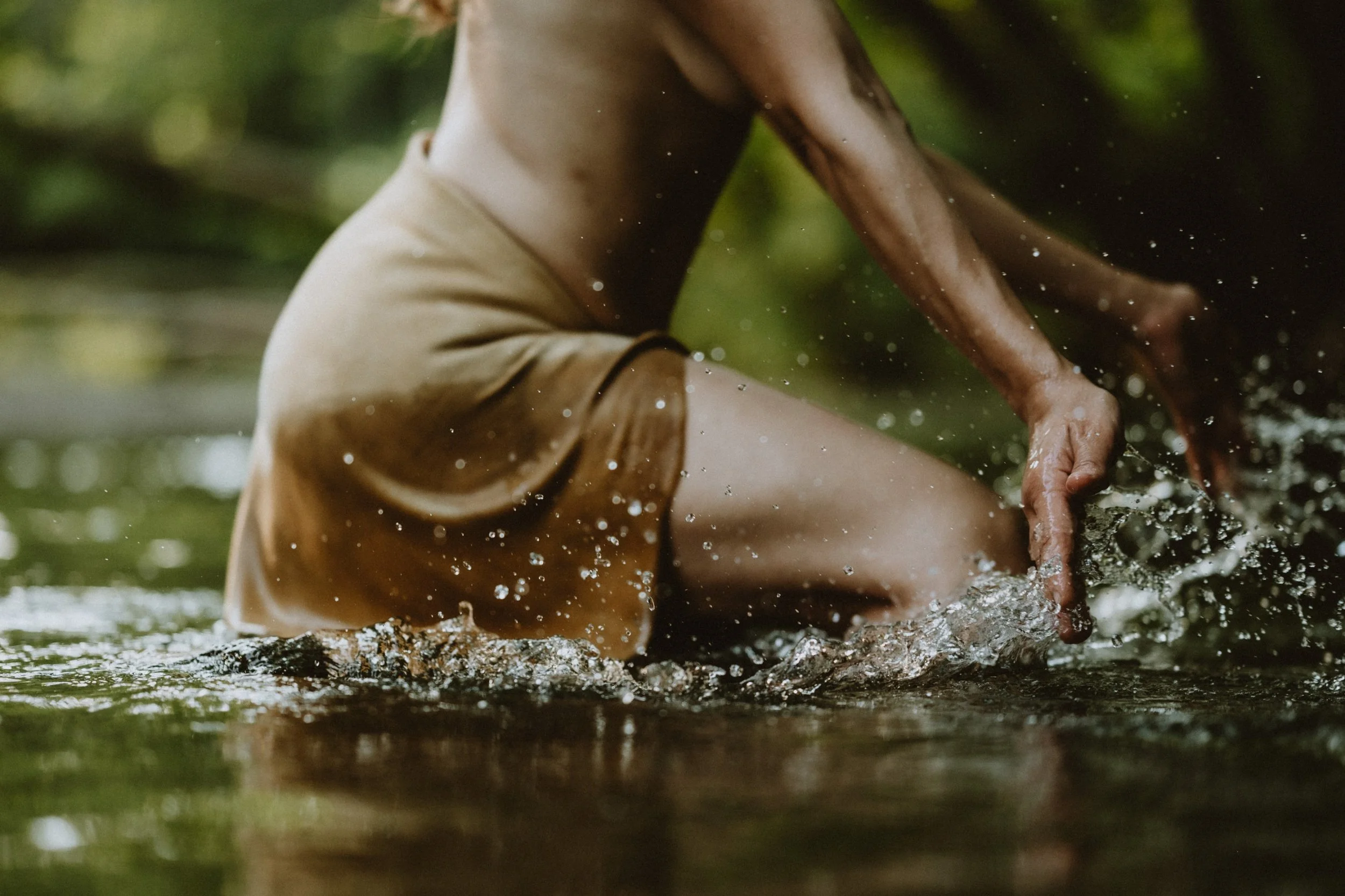 Person in a brown skirt splashing water in a creek or river