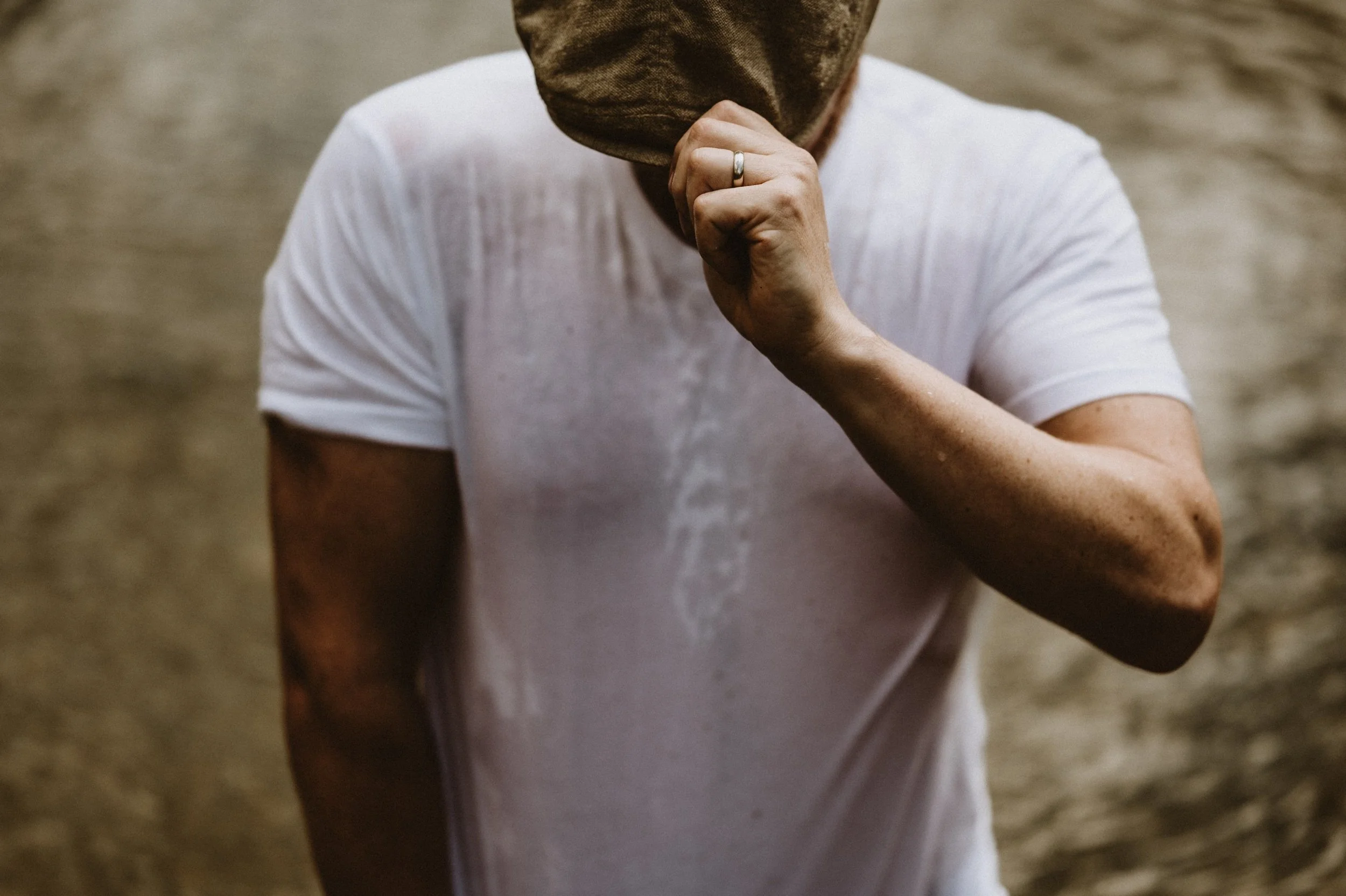 Person wearing a wet white t-shirt and adjusting a brown hat