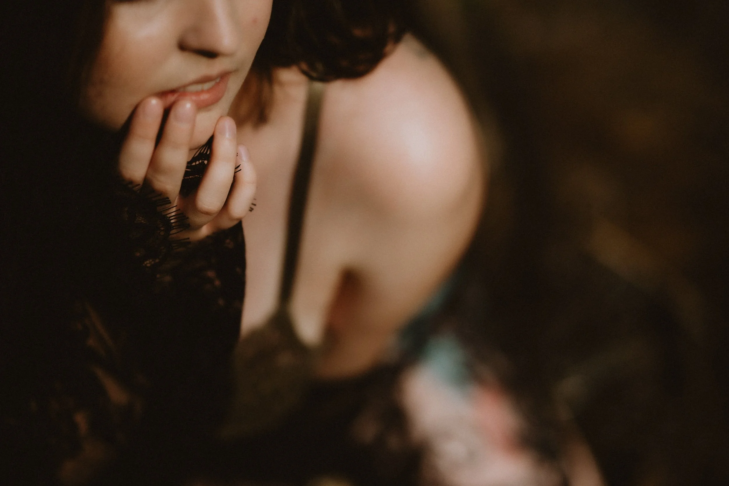 Close-up of a person with fingers near lips, wearing lace clothing, in soft focus.