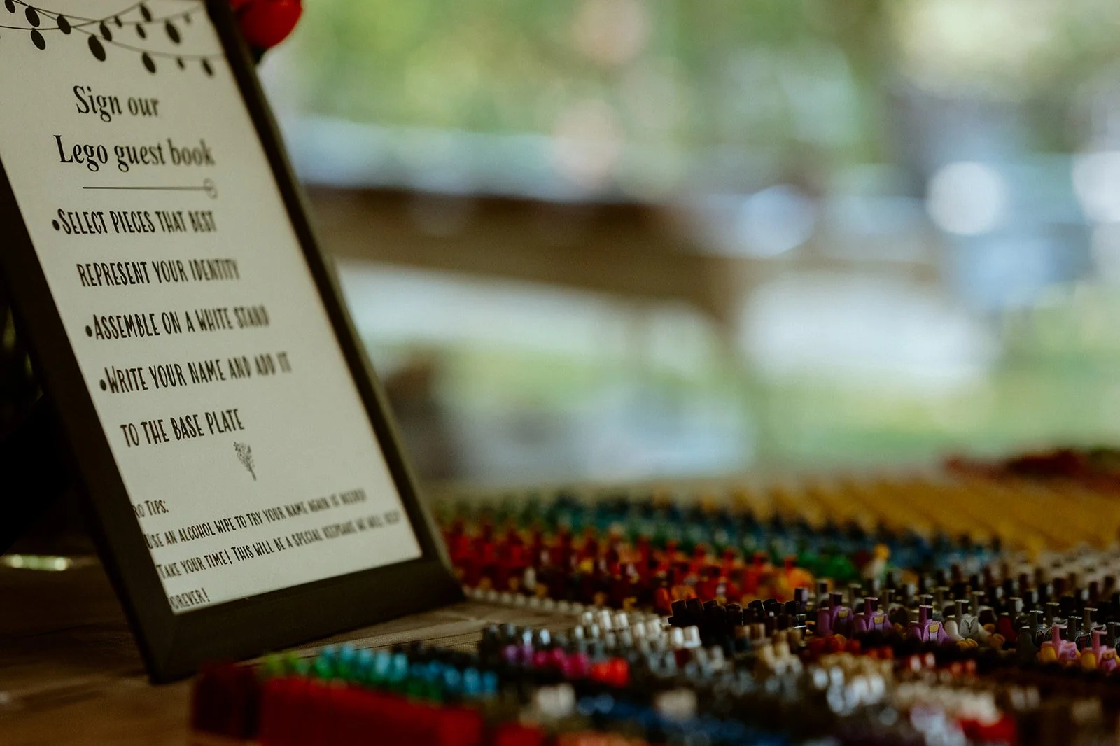 A framed sign for a Lego guest book next to neatly arranged Lego minifigure parts.
