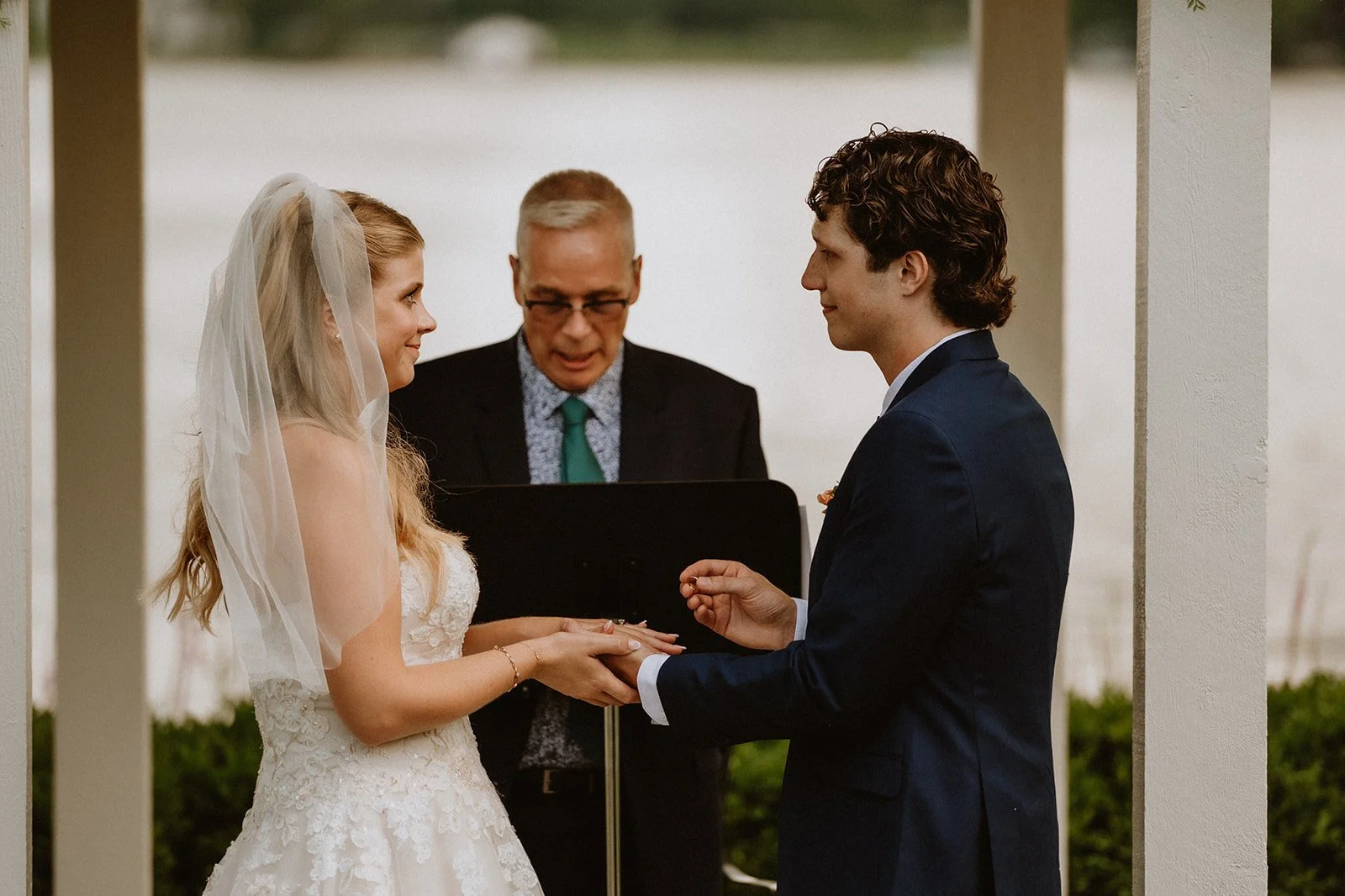 Bride and groom exchanging rings during an outdoor wedding ceremony with an officiant.