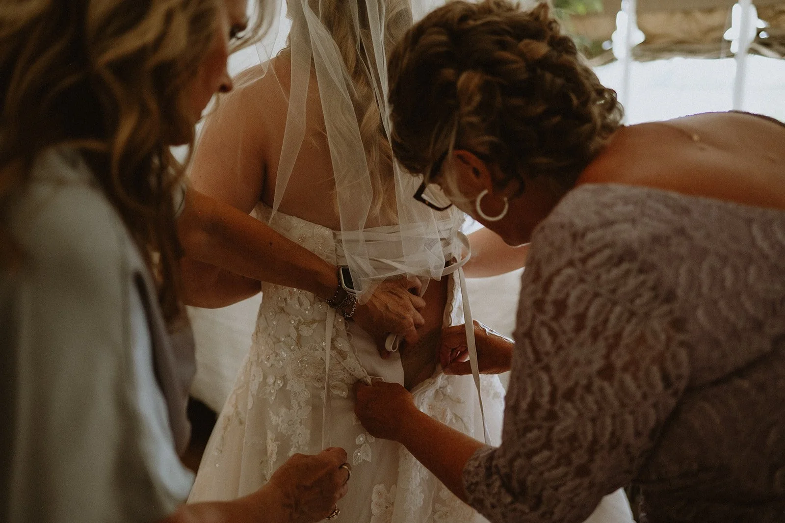 Bride getting help with dress adjustment before wedding ceremony.
