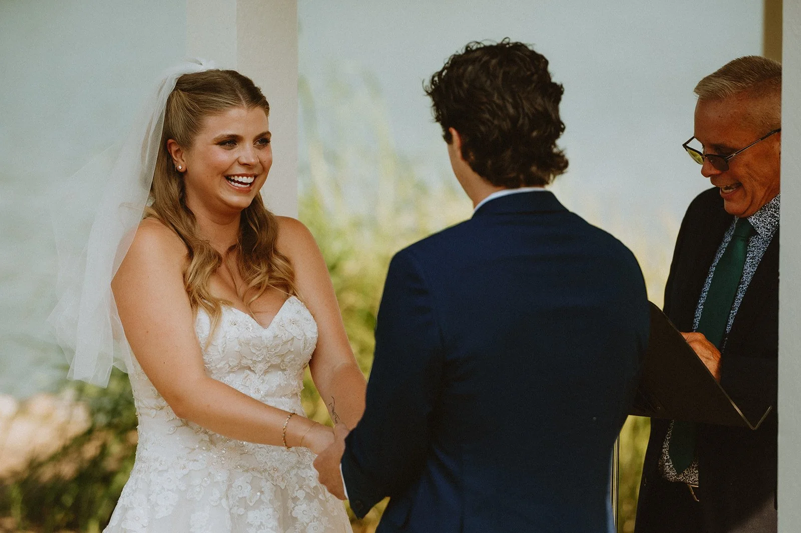 Bride and groom holding hands during wedding ceremony with officiant.