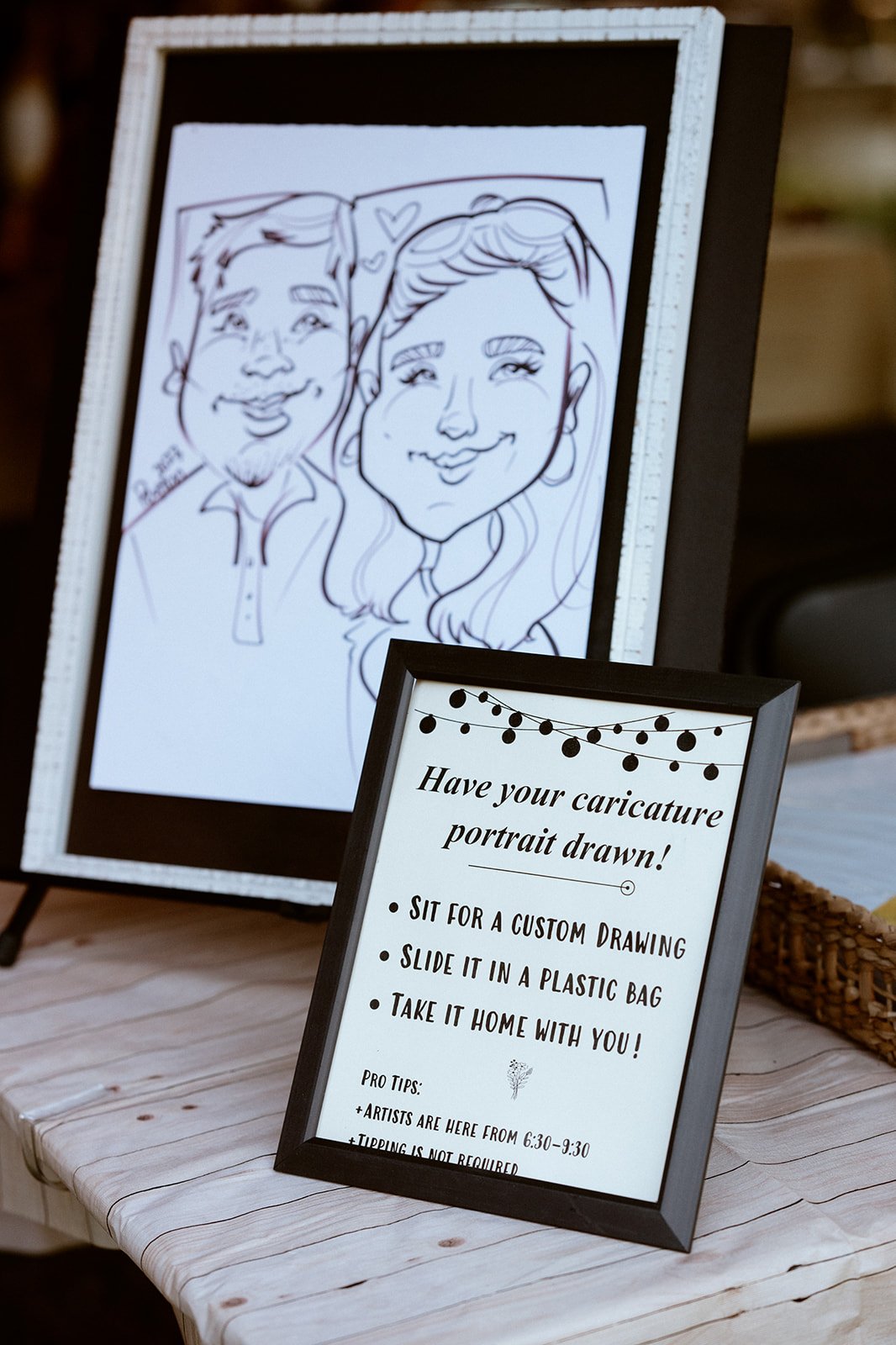 Caricature drawing displayed on an easel, alongside a framed sign that invites people to have their caricature portrait drawn. Instructions mention sitting for a custom drawing, placing it in a plastic bag, and taking it home. Artist hours and tippin