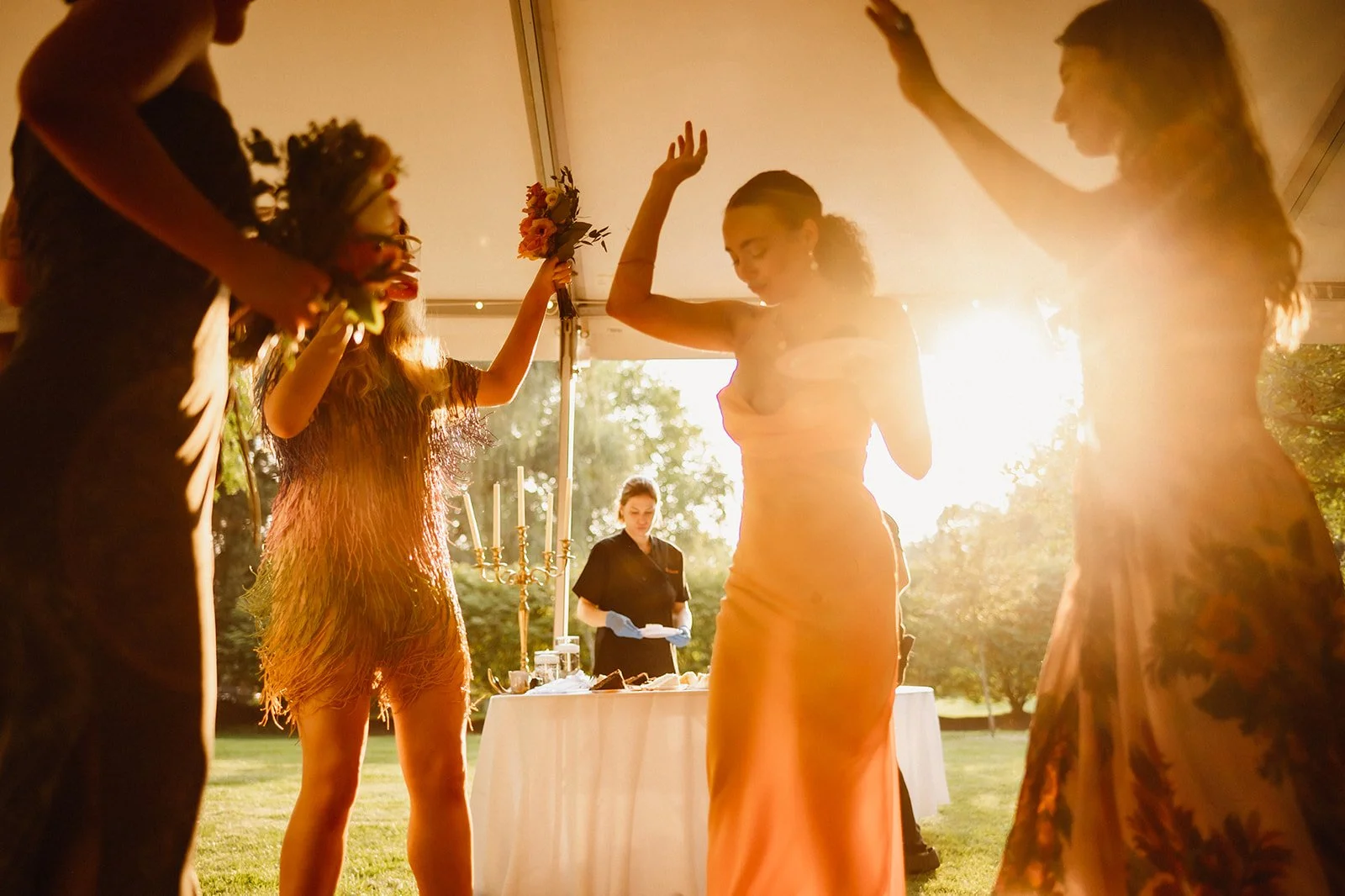 People dancing at an outdoor event during sunset, with a table and candles in the background.