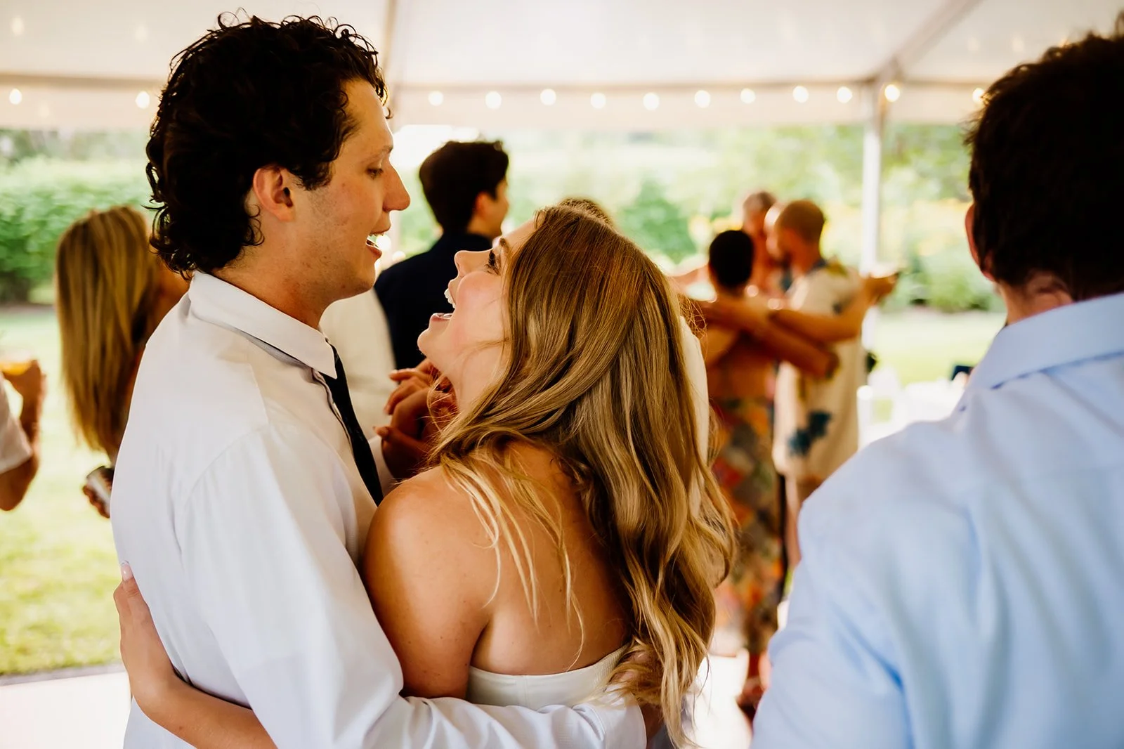 A couple dancing joyfully at an outdoor event with other people in the background.