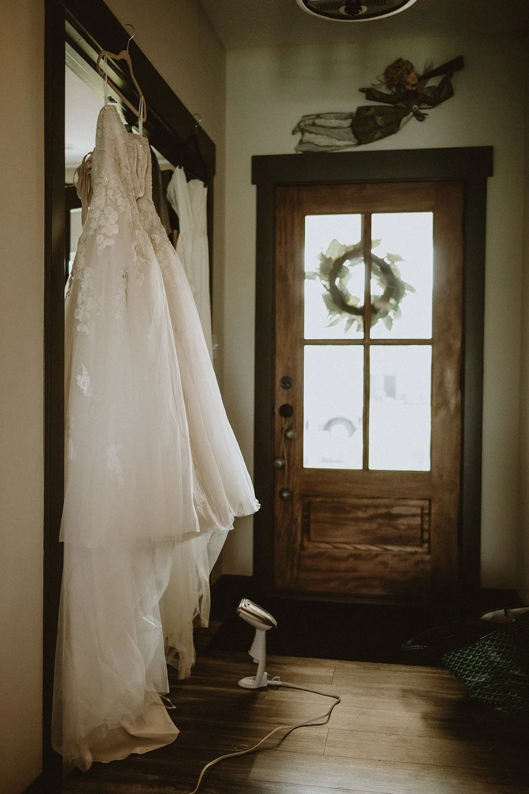 Wedding dress hanging on a door in a rustic room with wooden flooring.
