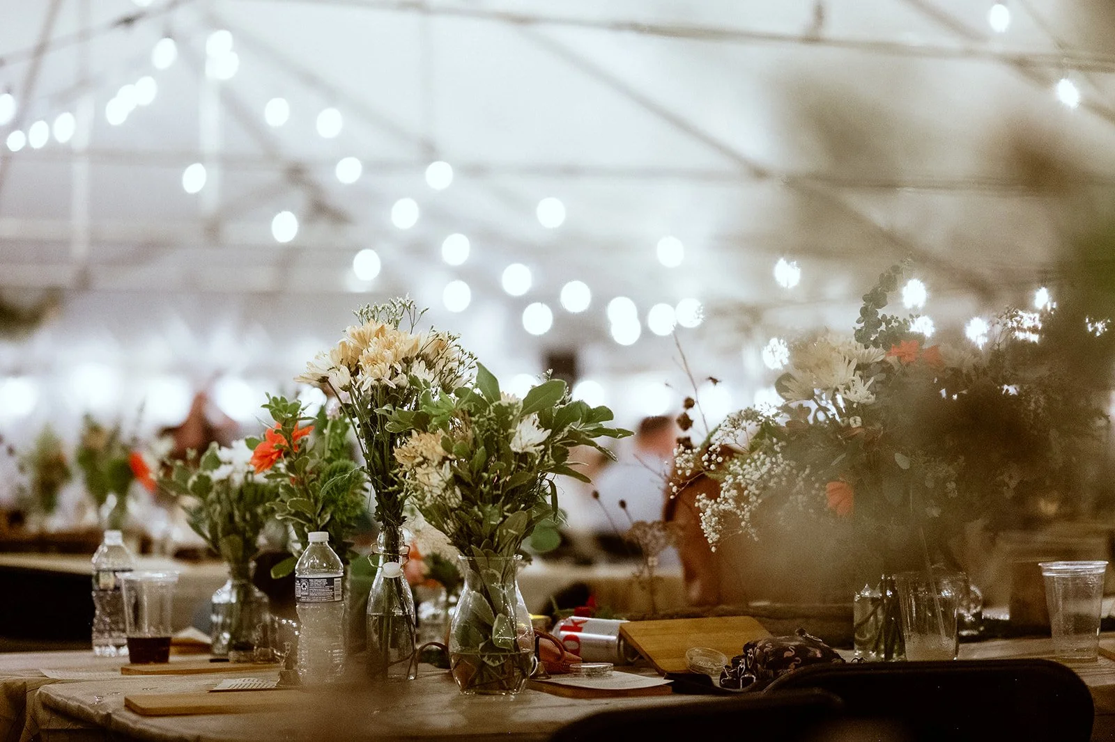 Flower arrangements on tables under a tent with string lights.
