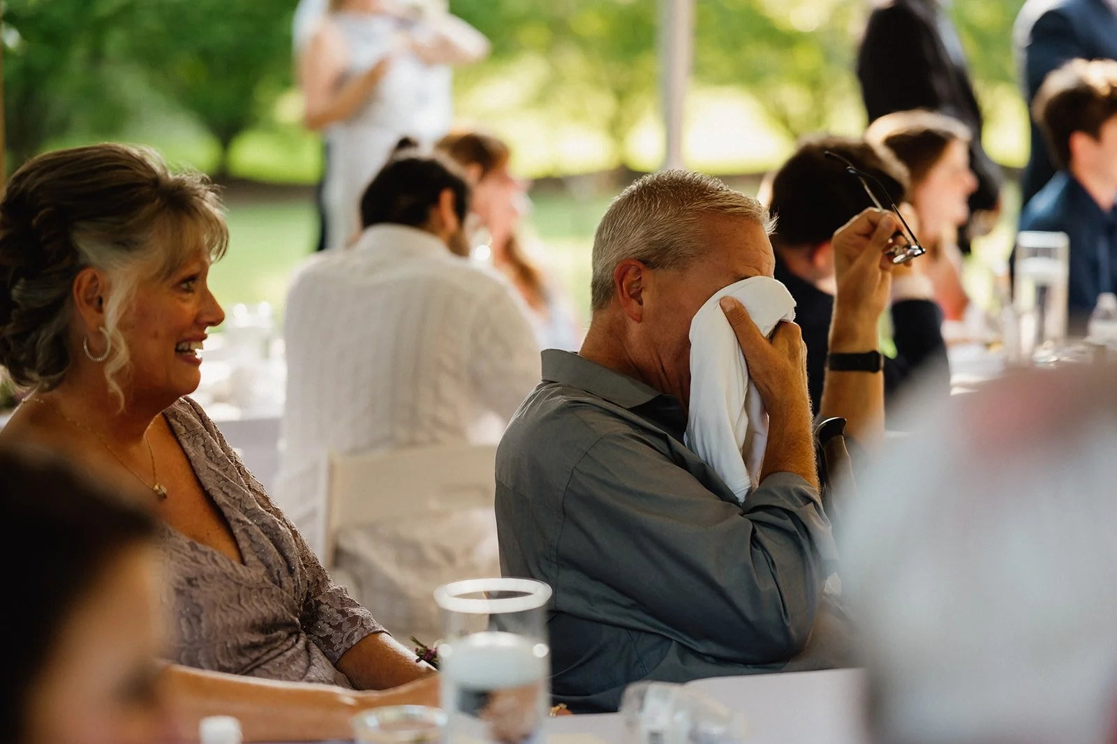 A man wiping his face with a cloth at a social gathering, seated next to a smiling woman.