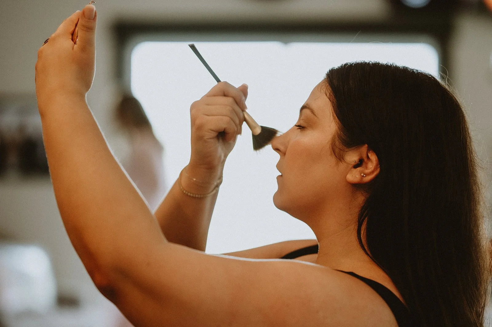 Woman applying makeup with brush in front of mirror.