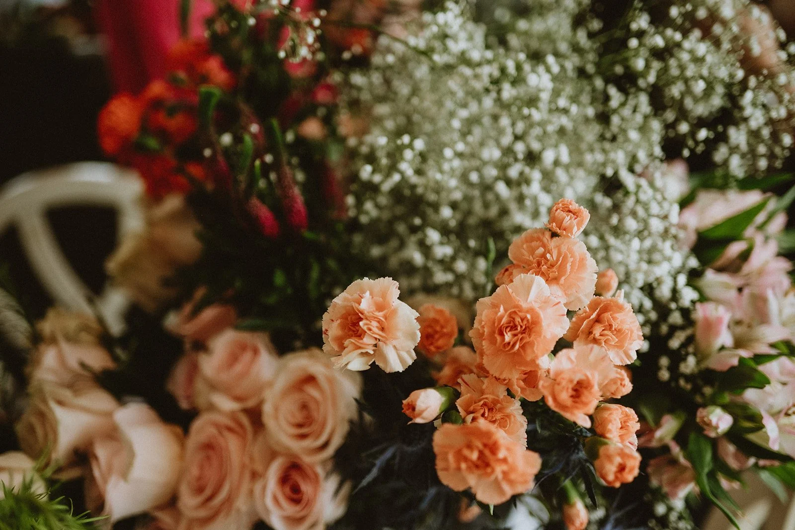 A floral arrangement featuring peach carnations, pink roses, and baby's breath.