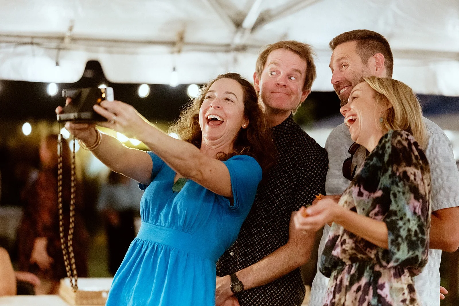 A group of four people smiling and taking a selfie under a tent at night.