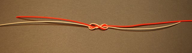 A double Surgeon's Knot before it's drawn tight. The orange line represents the leader (4X tippet material in this example) also known as the parent material. The white line represents the tippet material (5X tippet material in this example) being tied to the leader. Note that the tag end of 4X material lies alongside the tippet tippet material.