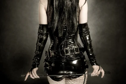 Woman wearing a black latex outfit with fishnet stockings and carrying a whip