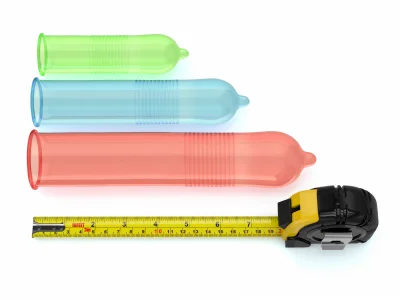 Three different length condoms unrolled next to a measuring tape