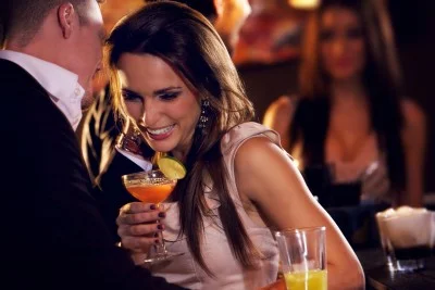 Man whispering something to a woman at the bar while she laughs
