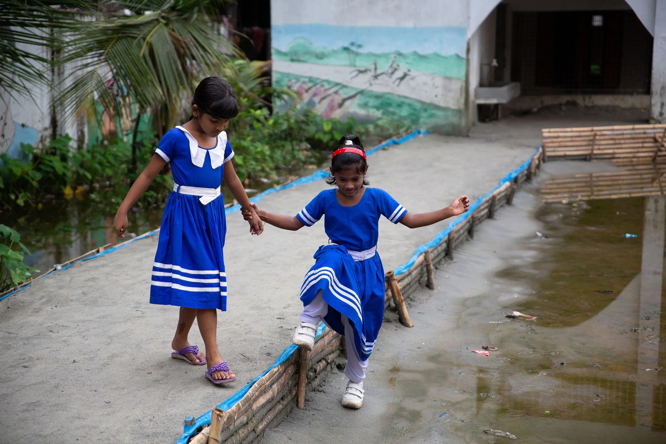 Girls help one another through flooded school courtyard, Nuru Chala Primary School.