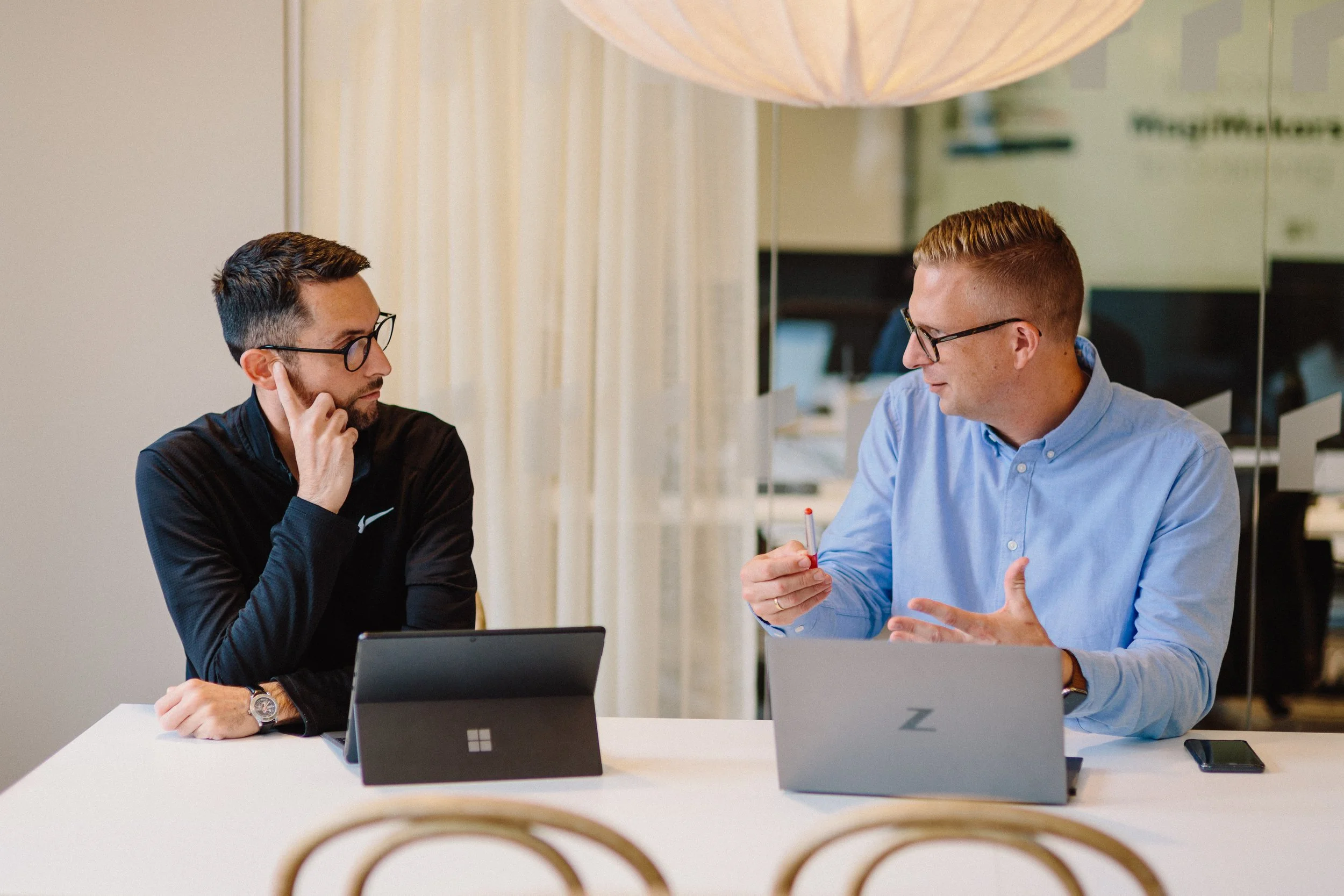 Två kollegor diskuterar framför laptops på kontor