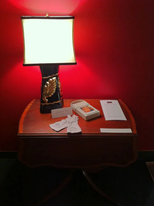 Spinster Style from Four Sisters . View of installation consisting of SX-70 Polaroid print mounted on Impossible Project white leather case, white leather gloves, text on menu card with original Russian Tea Room logo, and vintage lamp. In “Our House!: Portraiture and the Queering of Home,” curated by Lex Lancaster, Evolution Arts Collective, October 2012.