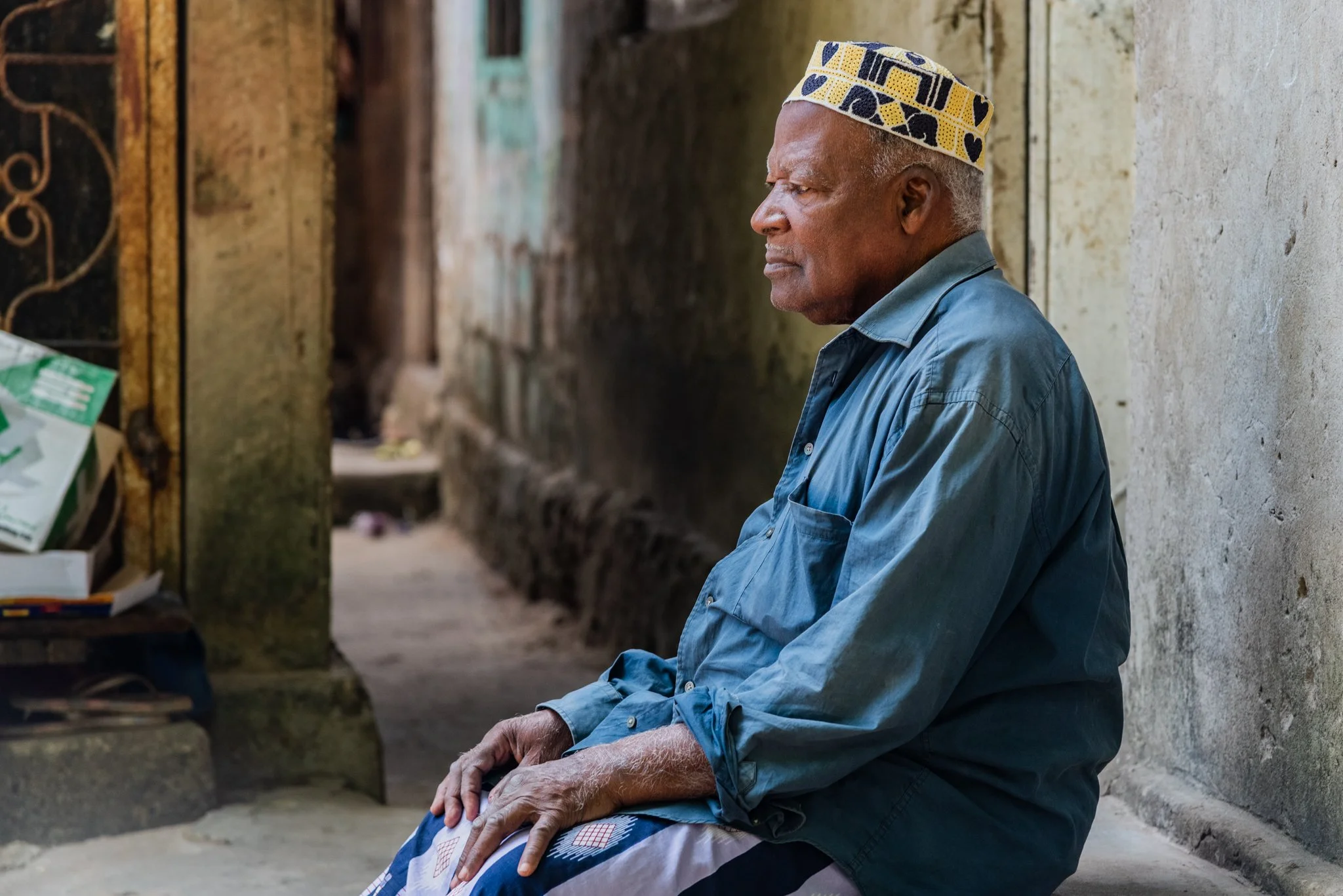 An elderly man is sitting on a concrete bench outside his home in Zanzibar, Tanzania.