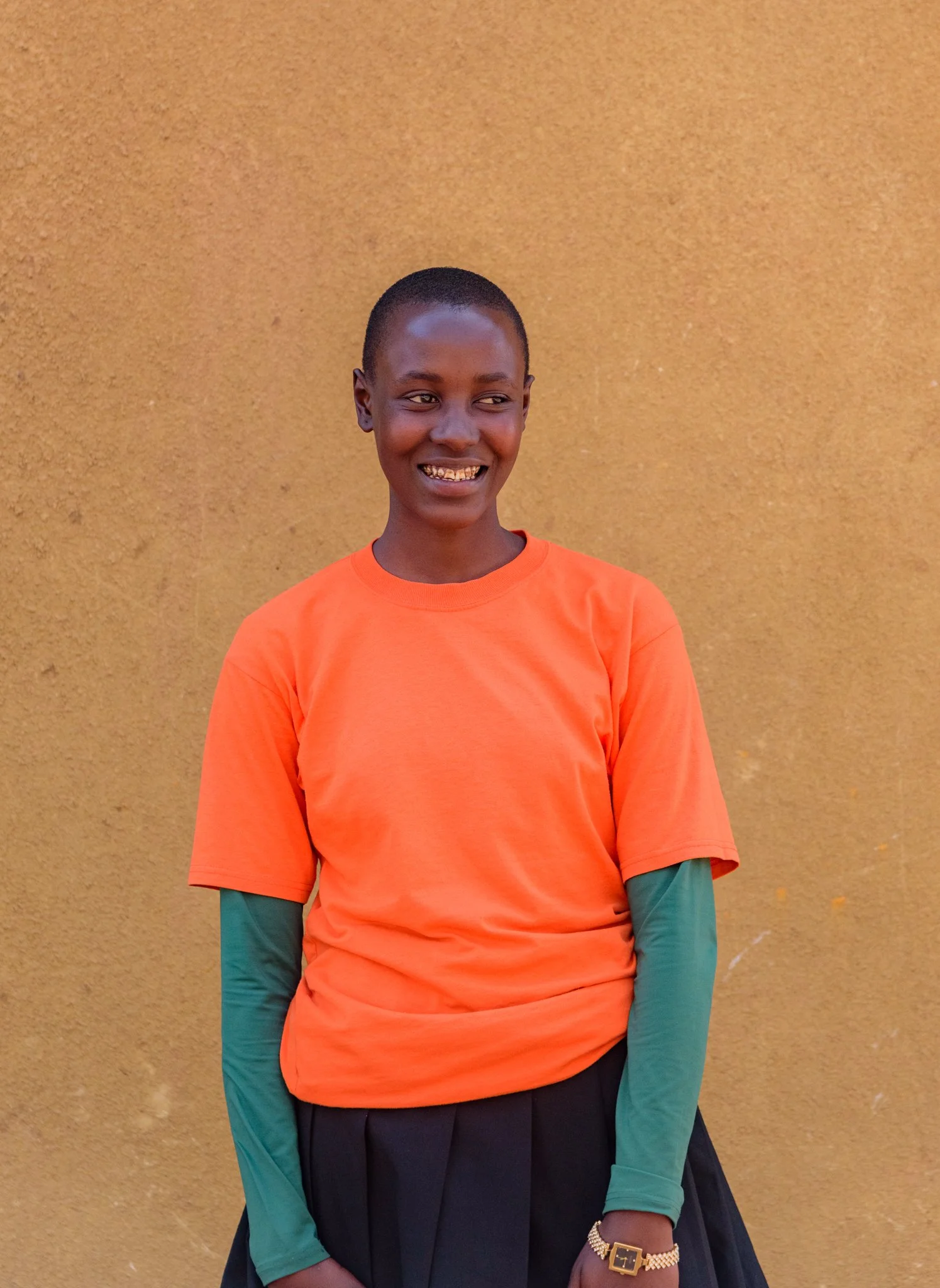 Portrait of a smiling Tanzanian secondary schoolgirl standing in front of a wall in Arusha, Tanzania, photographed for the Malala Fund.